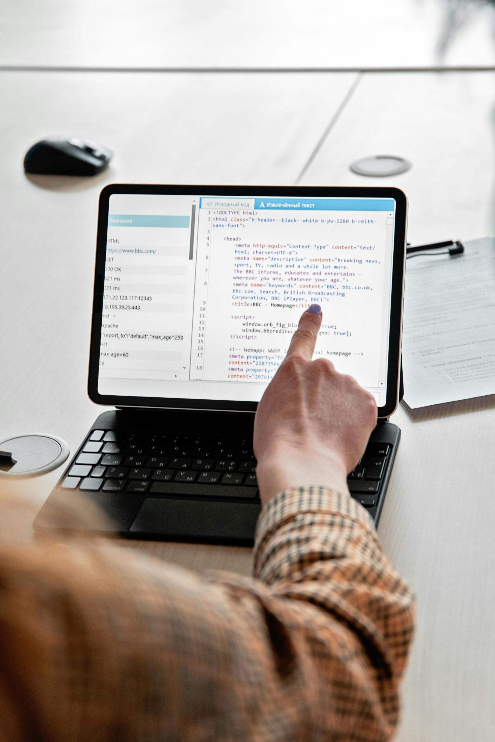 Persona señalando código HTML en tableta con teclado, revisando estructura técnica de página web durante sesión de aprendizaje de programación y desarrollo web.