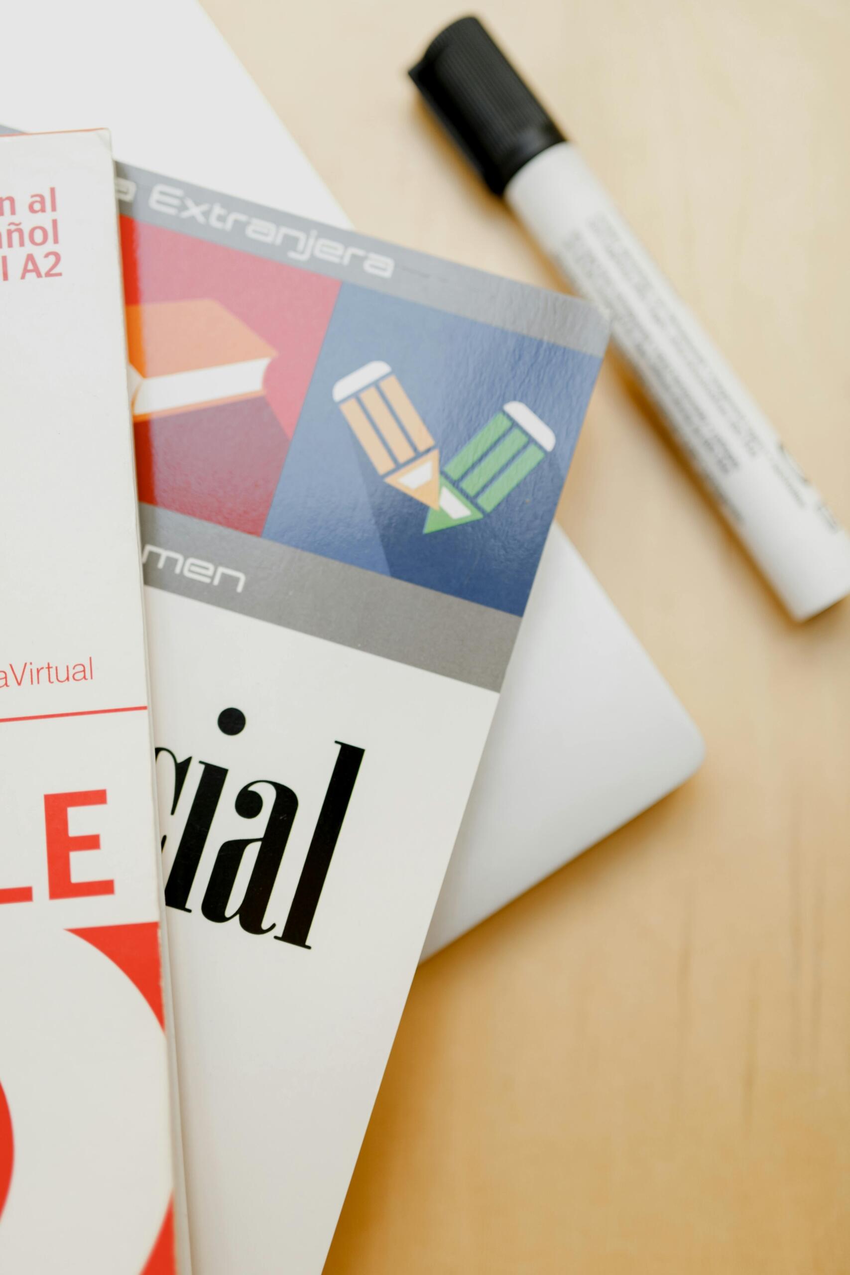 Libros de español como lengua extranjera nivel A2 sobre escritorio de madera junto a marcador blanco, ideales para aprender idiomas con clases particulares online.
