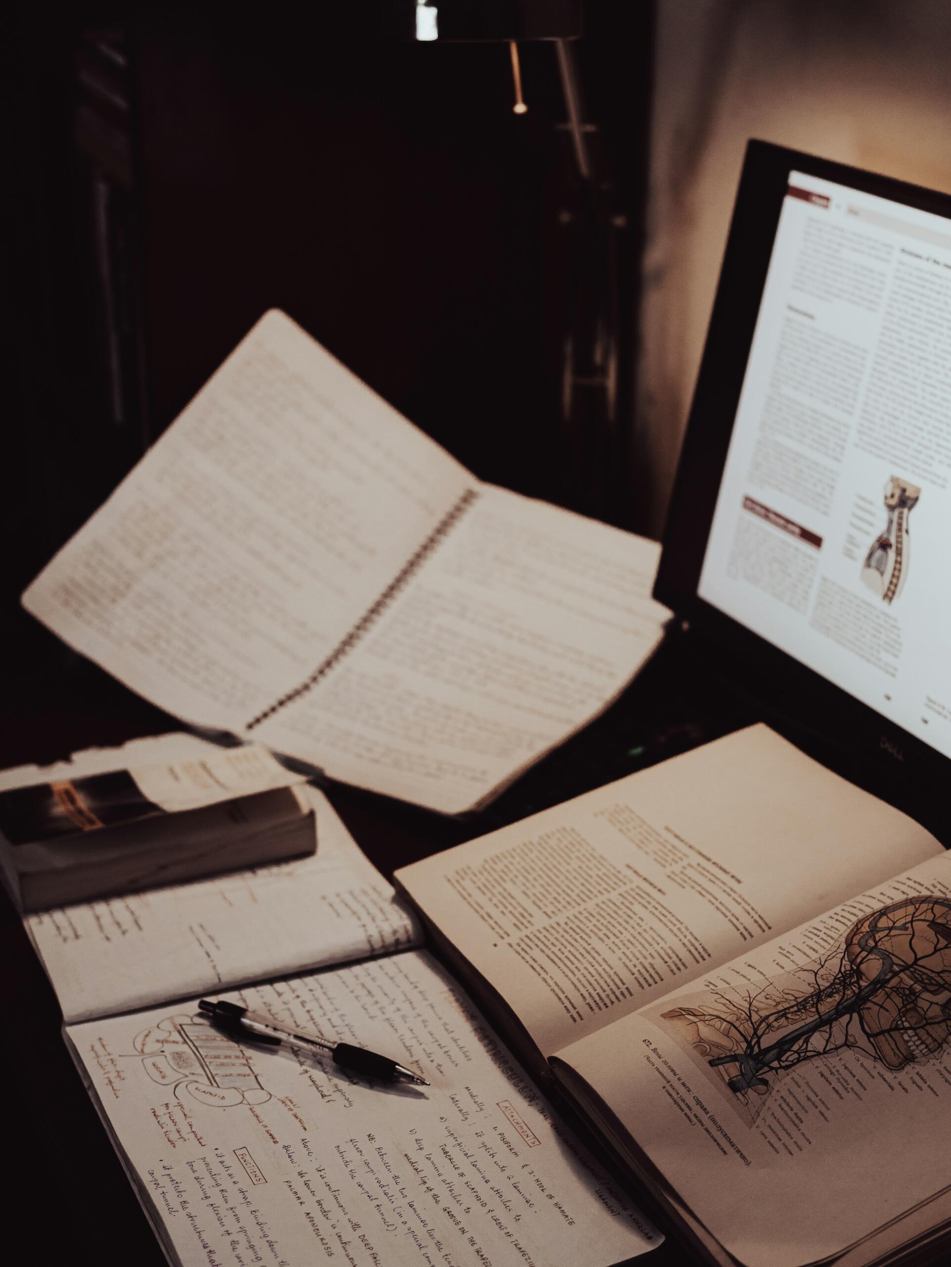 Escritorio de estudio de biología con apuntes, libro de anatomía y monitor.