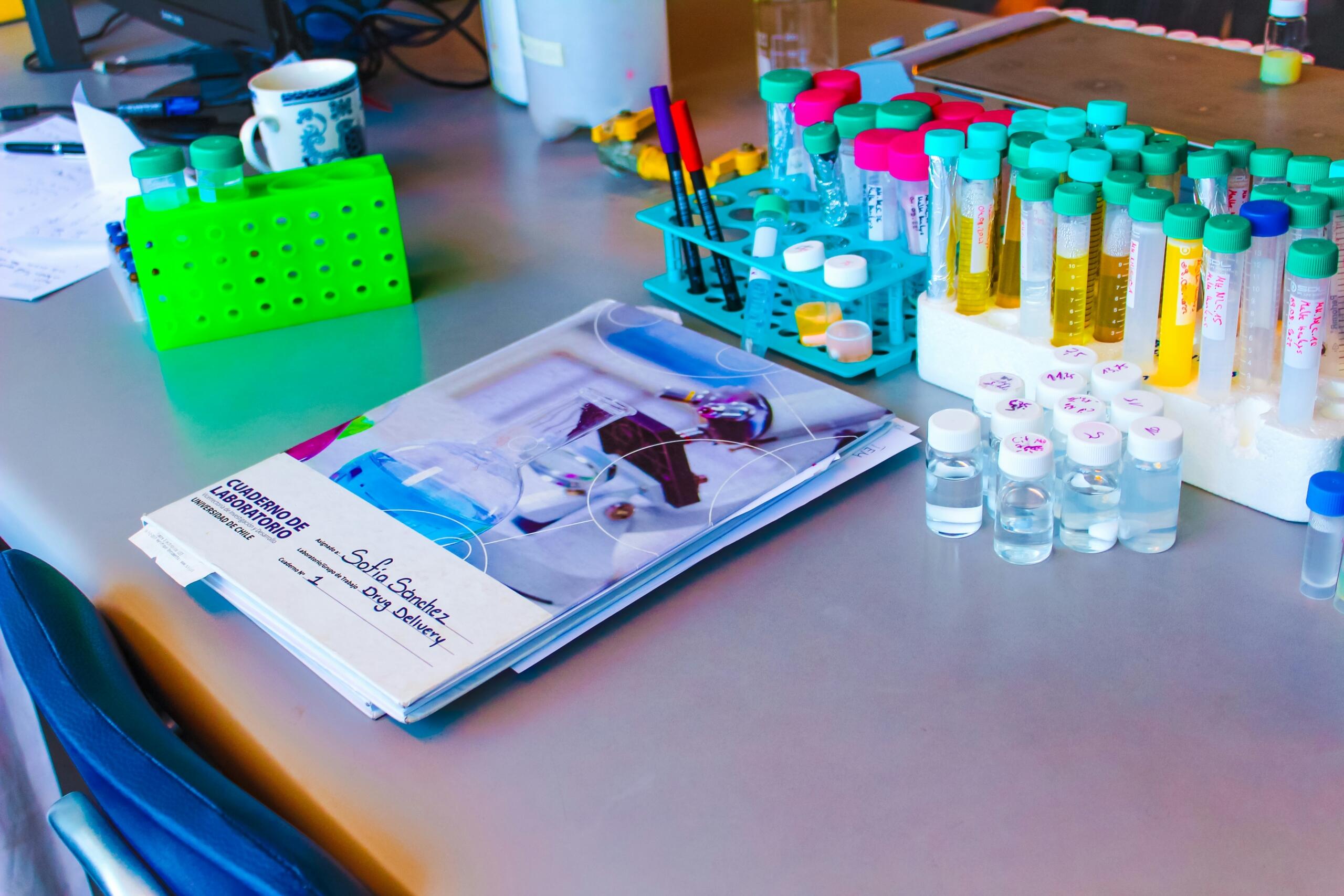 Cuaderno de laboratorio y tubos de ensayo en una mesa de trabajo de biología.