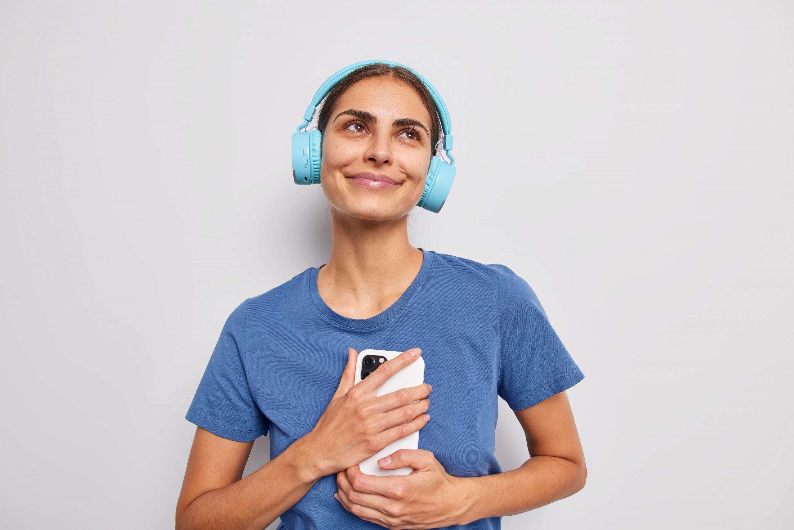 chica sonriente con audifonos y un telefono en la mano mirando hacia arriba