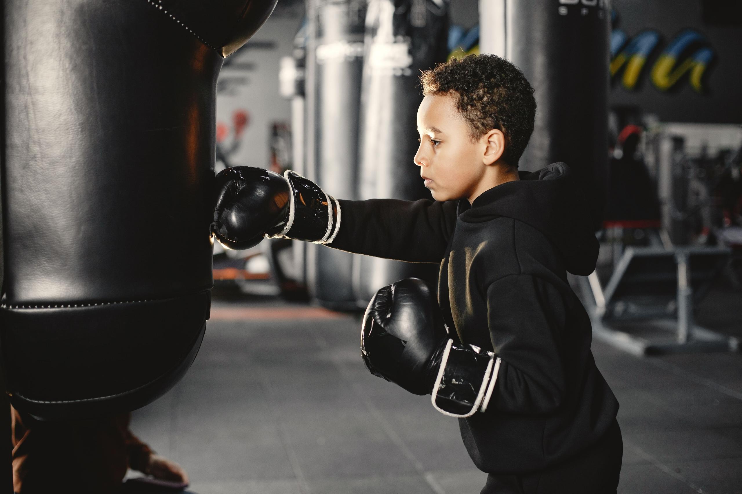 niño con guantes negros golpeando un saco de boxeo