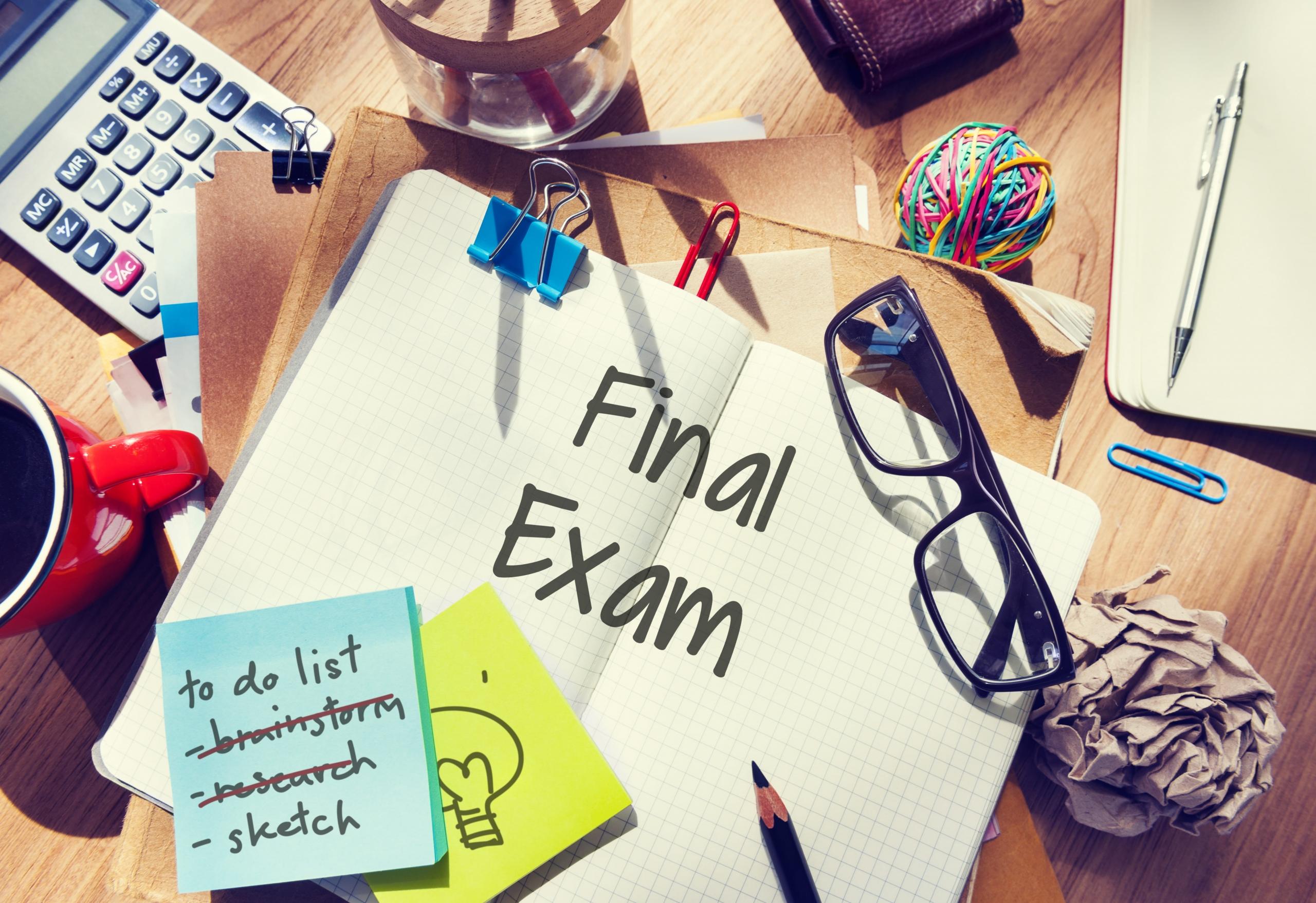 cuaderno abierto con la frase FINAL EXAM con post its, papeles y lapiceros alrededor de la mesa