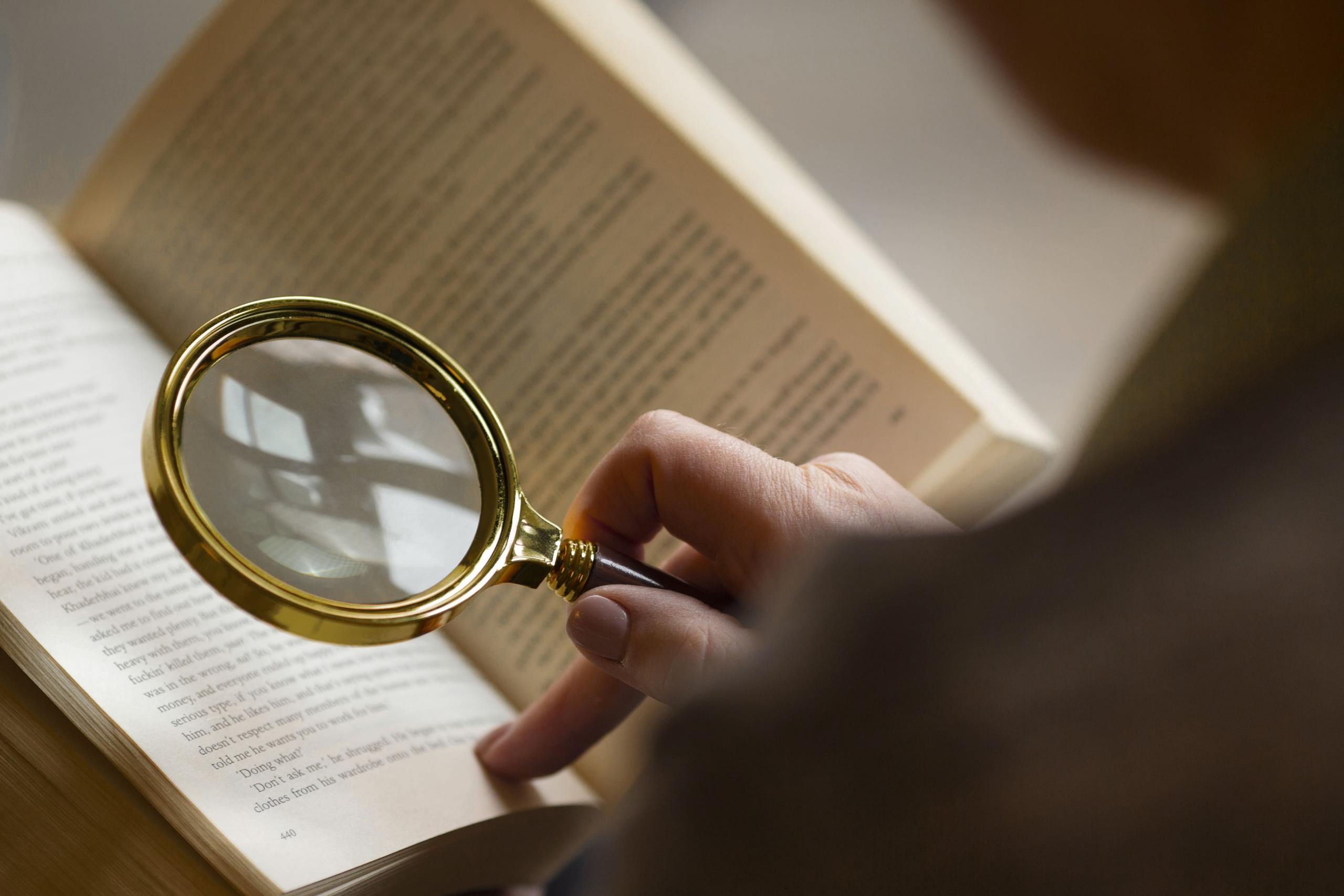 persona leyendo un libro de inglés con una lupa en su mano