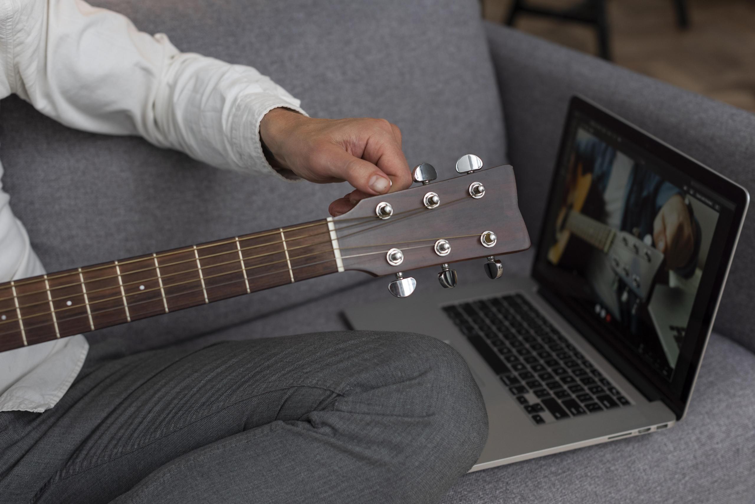 chico con una guitarra mirando clase de guitarra en su laptop