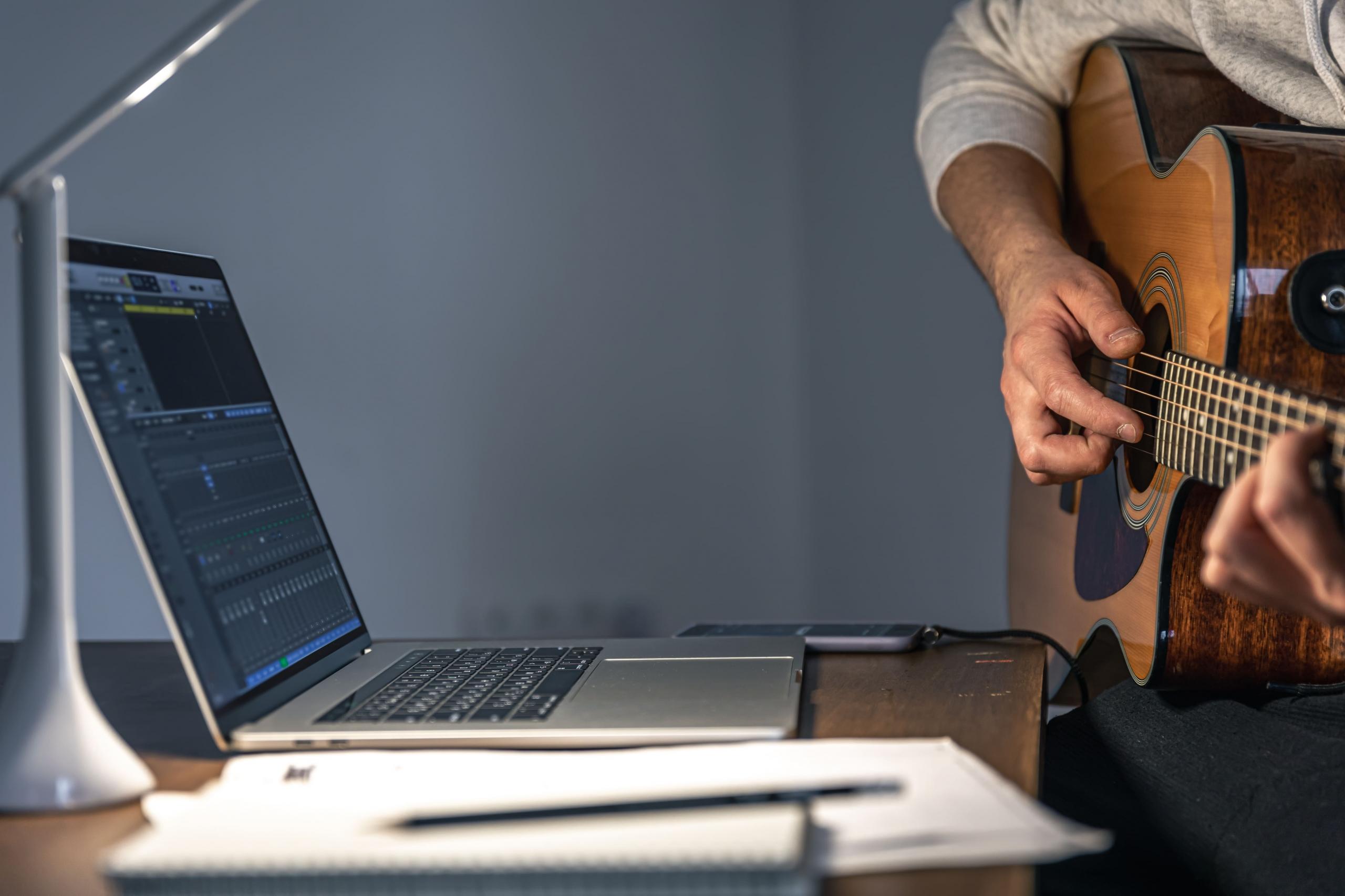 persona tocando la guitarra frente a una laptop