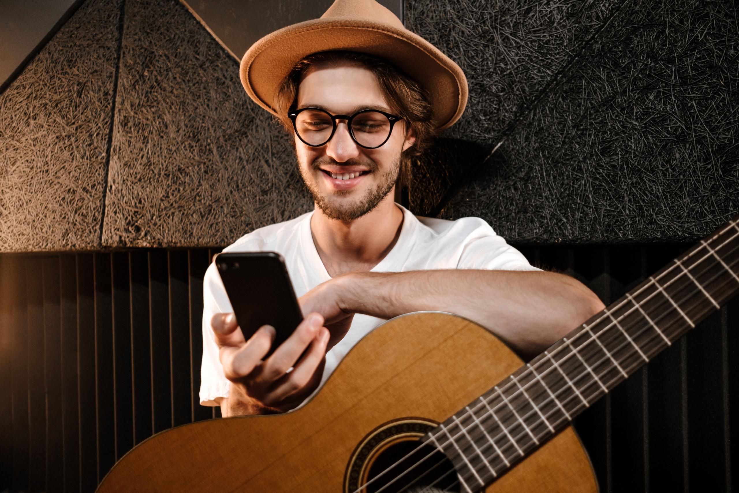 chico mirando su celular con una guitarra encima