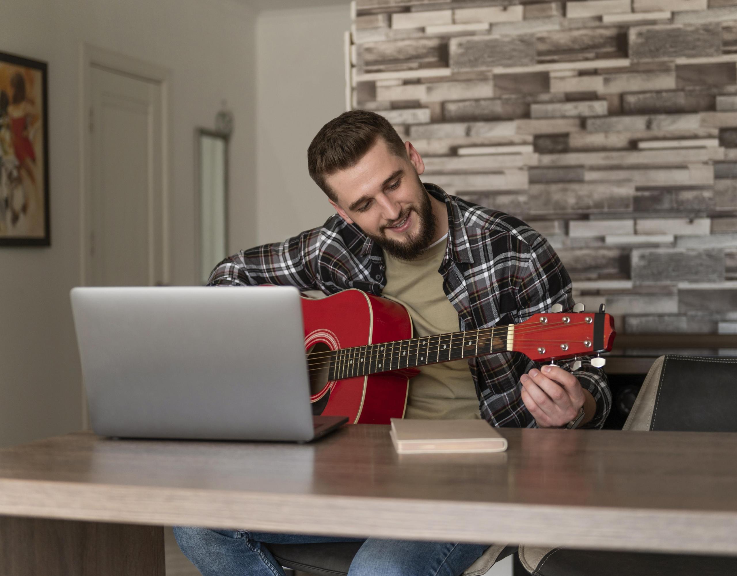 chico tocando la guitarra con una laptop sobre la mesa