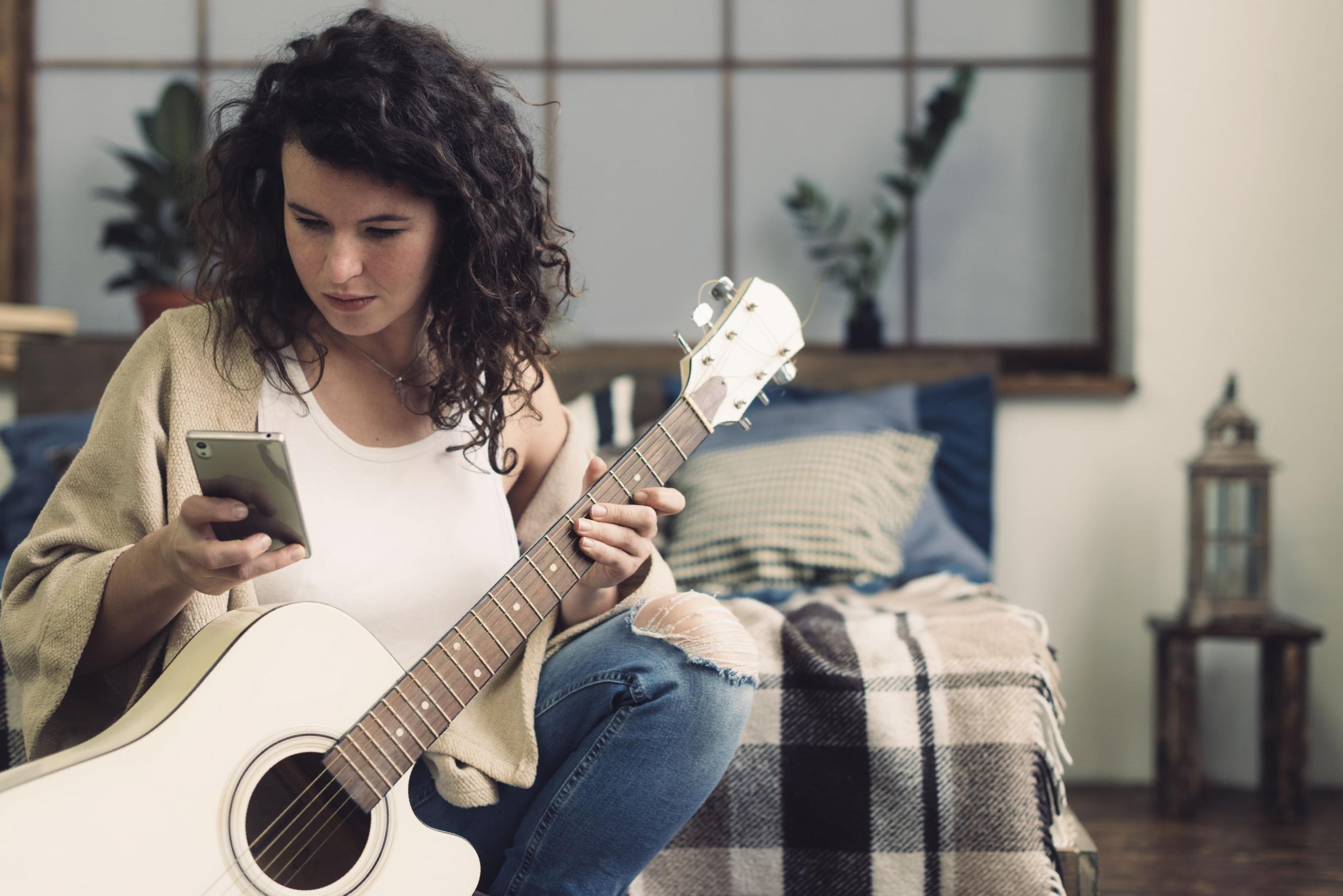 mujer con una guitarra y leyendo su celular