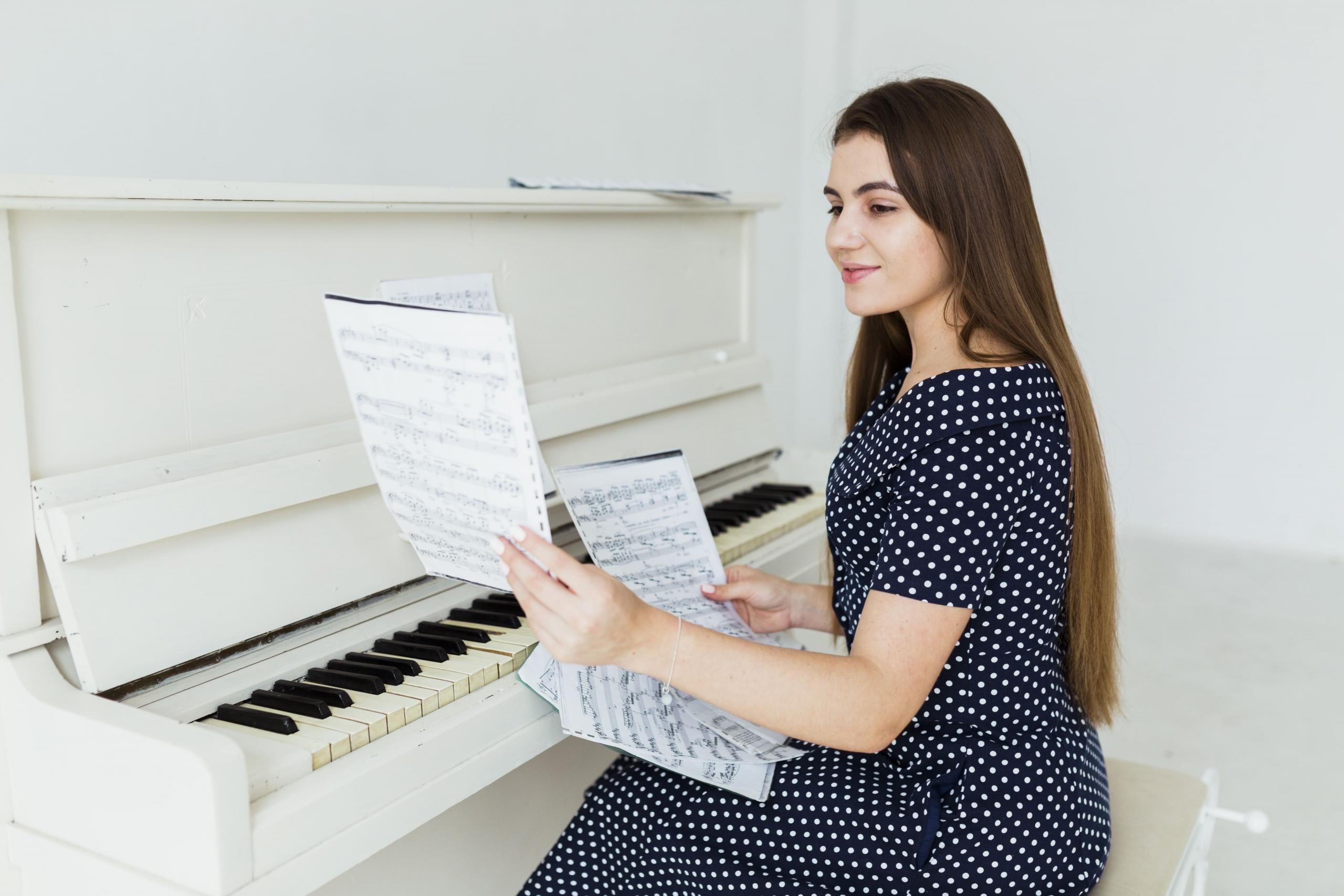 chica sentada frente a un piano blanco y leyendo unas partituras para tocar