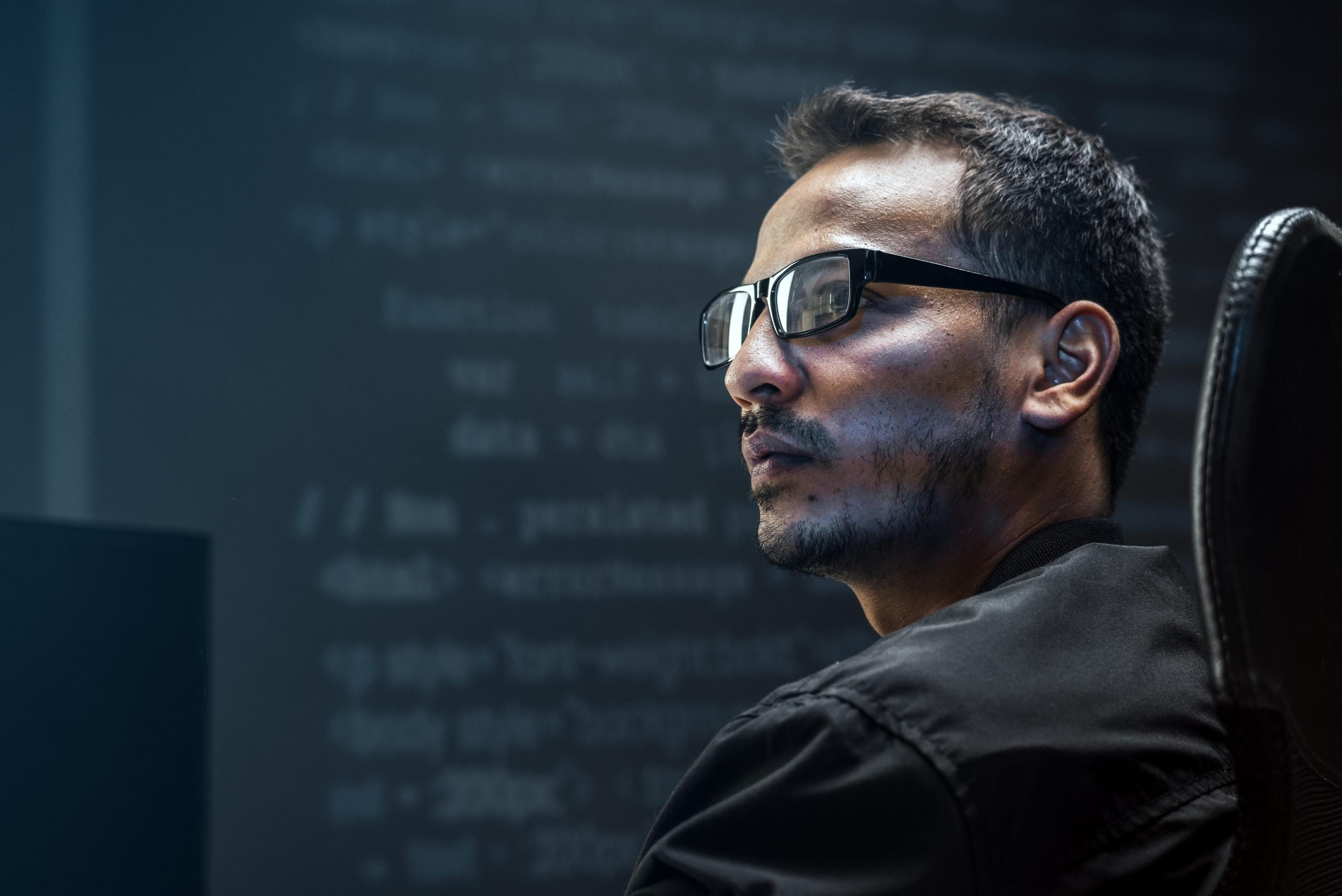 reflejo de codigos de programacion sobre el rostro de un hombre con lentes mirando de perfil