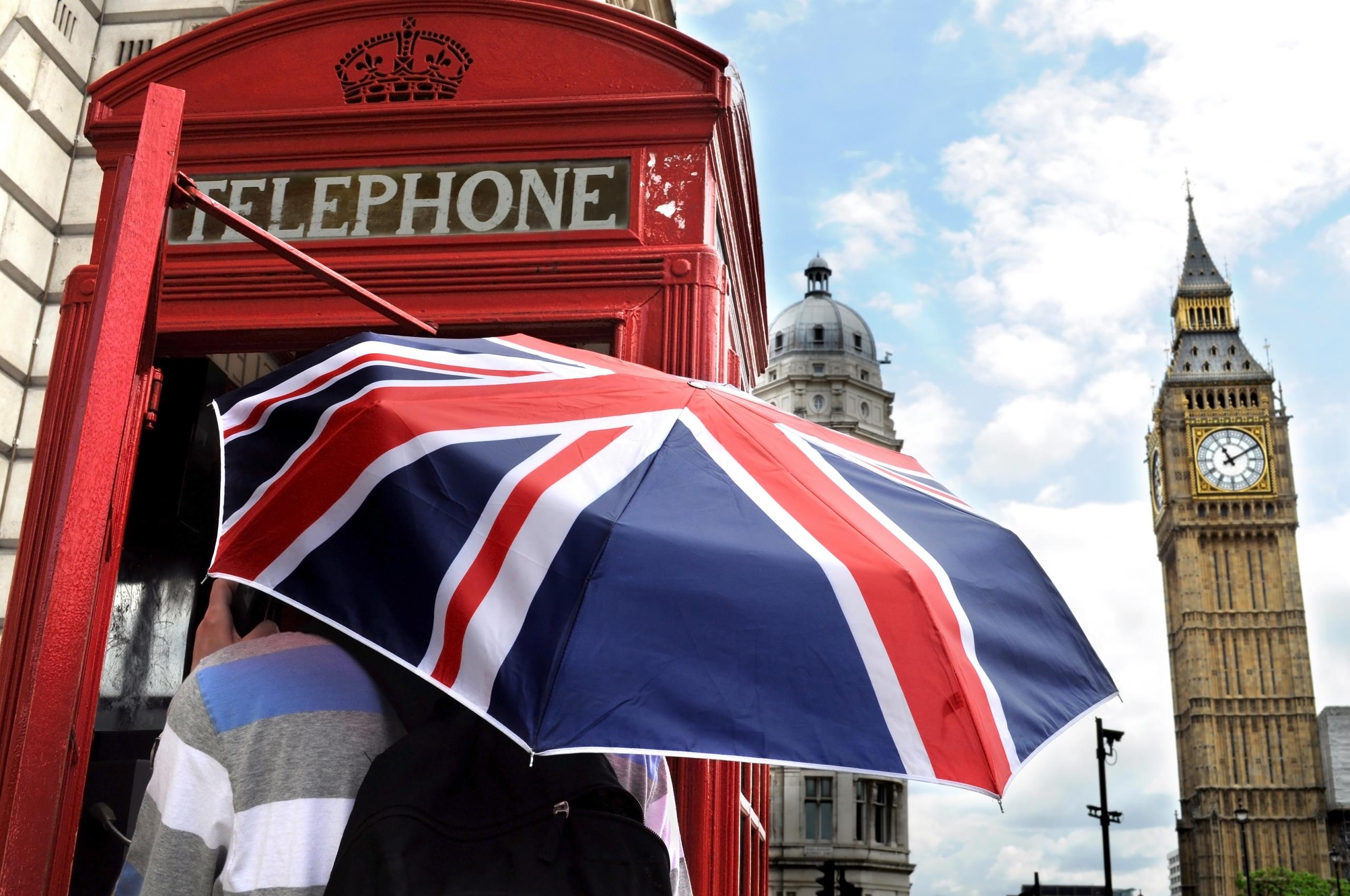 persona con paraguas de la bandera de inglaterra en una cabina de telefono roja y el big ben a la vista
