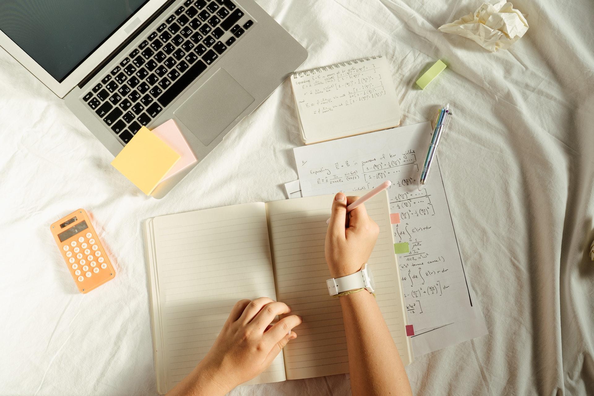 Mujer sobre la cama calculando sus finanzas, con una laptop y una calculadora