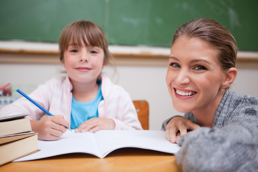 profesora junto a su alumna mirando a la cámara sonrientes mientras estudian