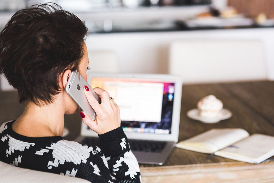 mujer hablando por telefono en su escritorio con laptop y un libro en la mesa
