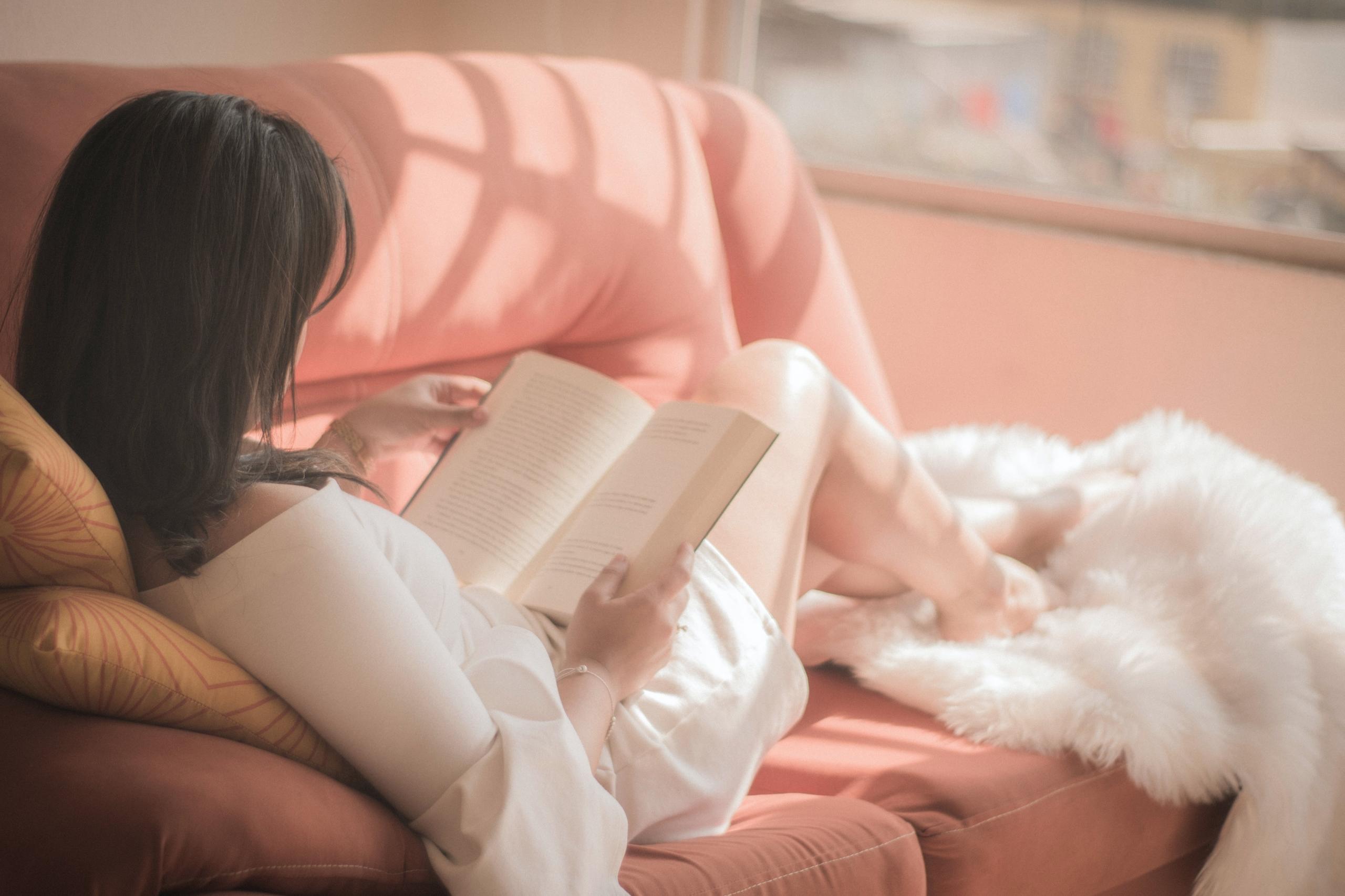 chica leyendo un libro mientras descansa sobre un sofa