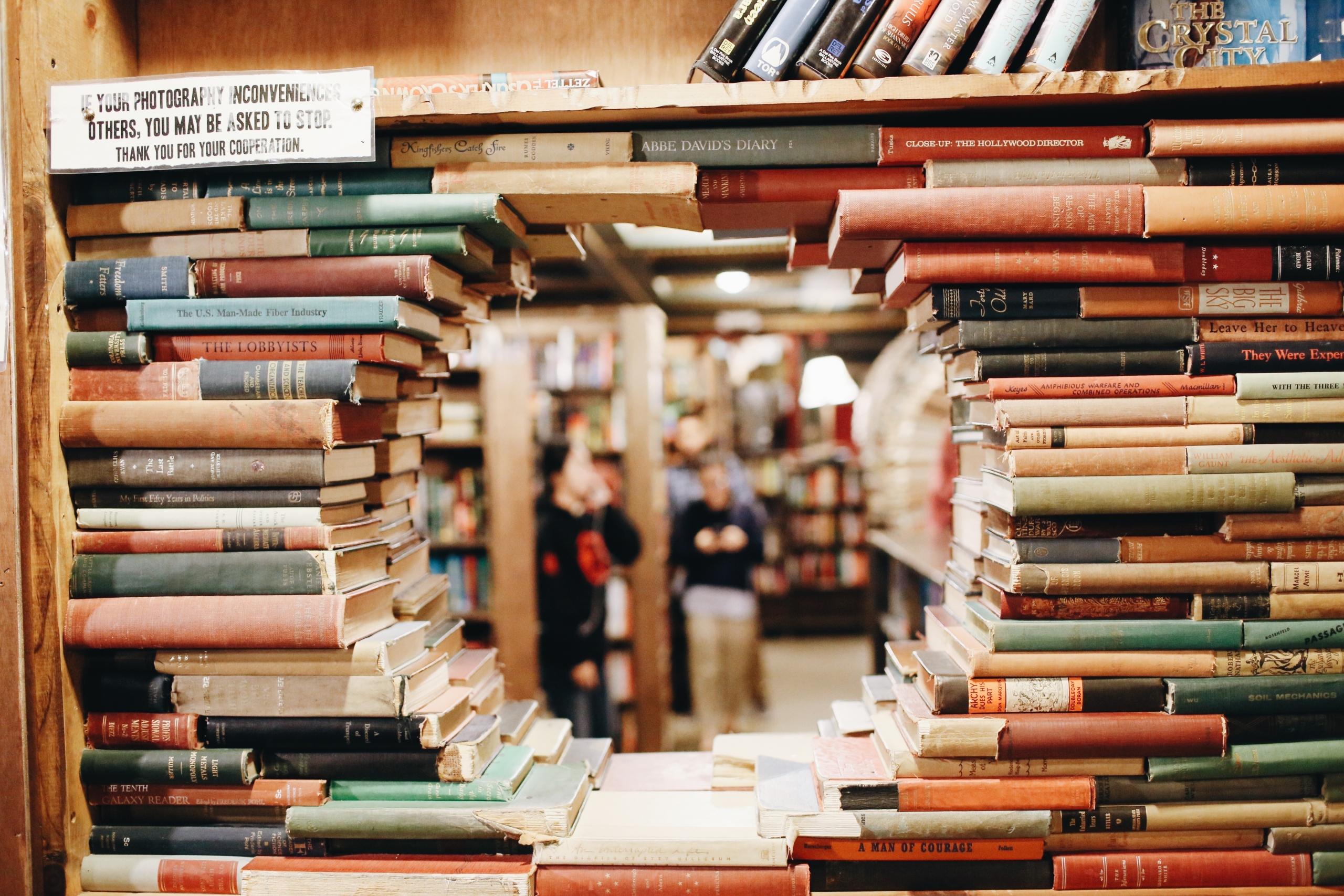 muro de libros apilados en estanteria con un agujero en medio en el que se ve las otras columnas de la biblioteca