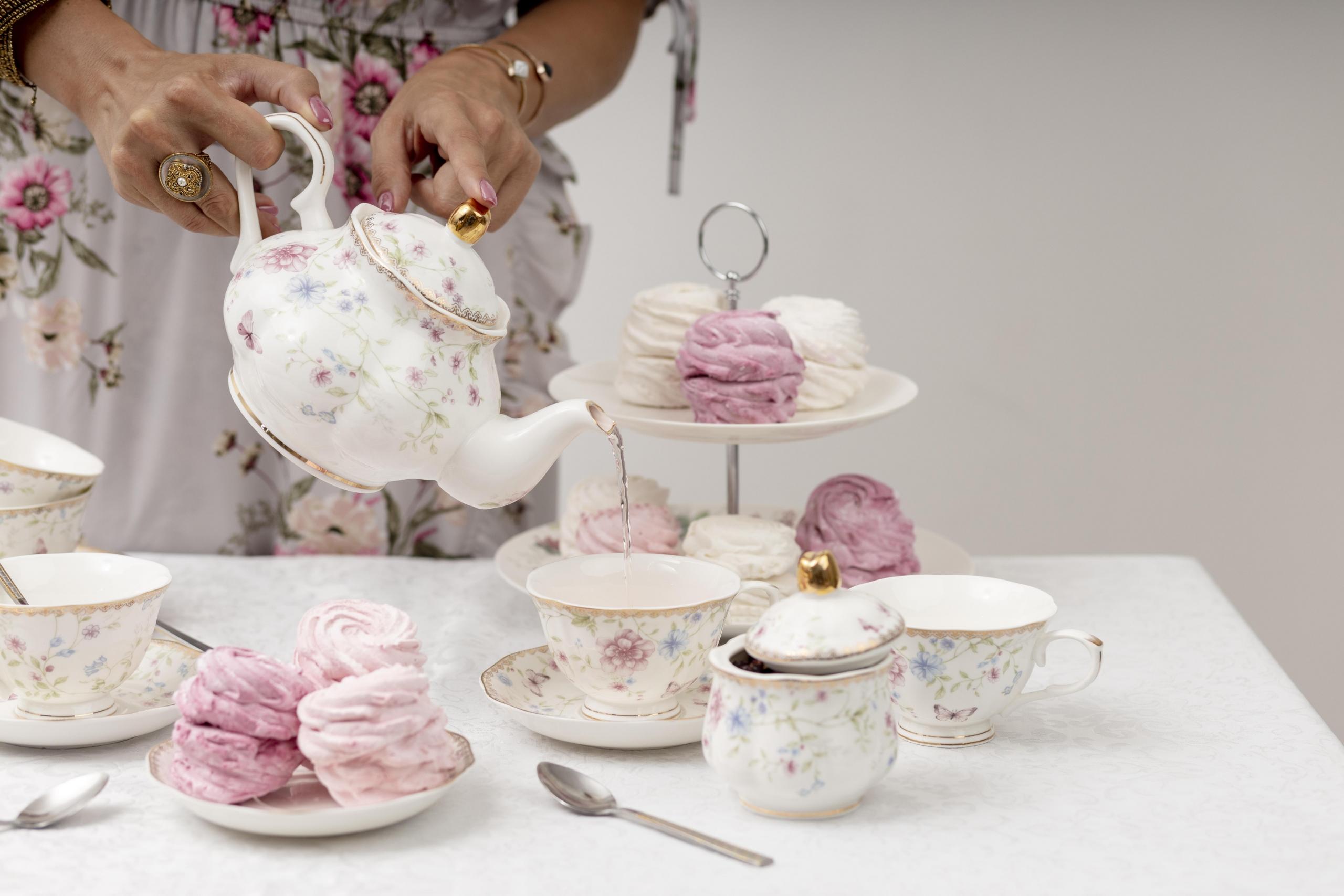 mesa armada con delicadas vajillas inglesas y una mujer sirviendo una taza de té