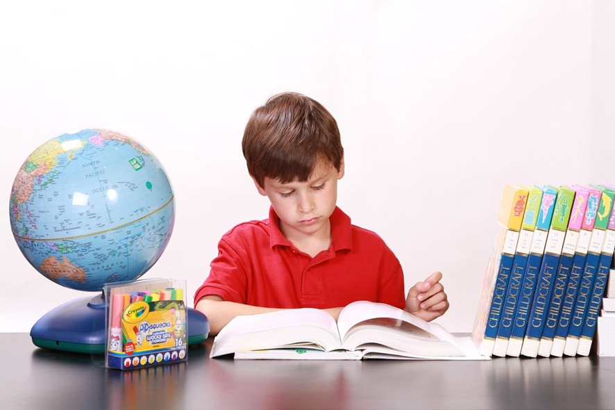 Niño leyendo un libro de inglés junto a un globo terráqueo, caja de plumones y otros tomos de libros de inglés