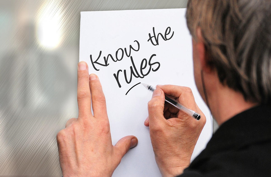 hombre de espaldas escribiendo sobre una hoja KNOW THE RULES