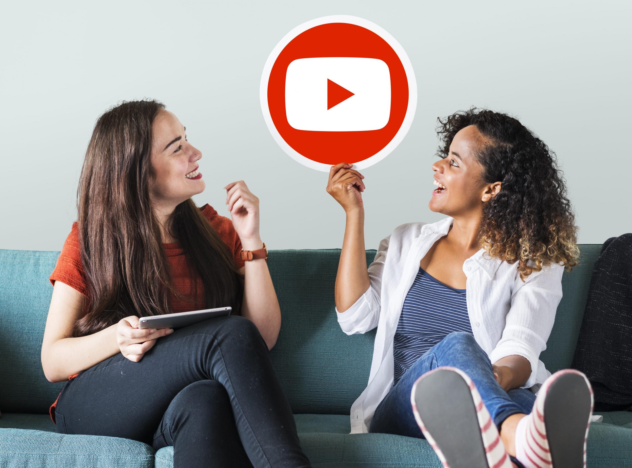 mujer sosteniendo un cartel con el logo de Youtube y su amiga mirando sonriente hacia este