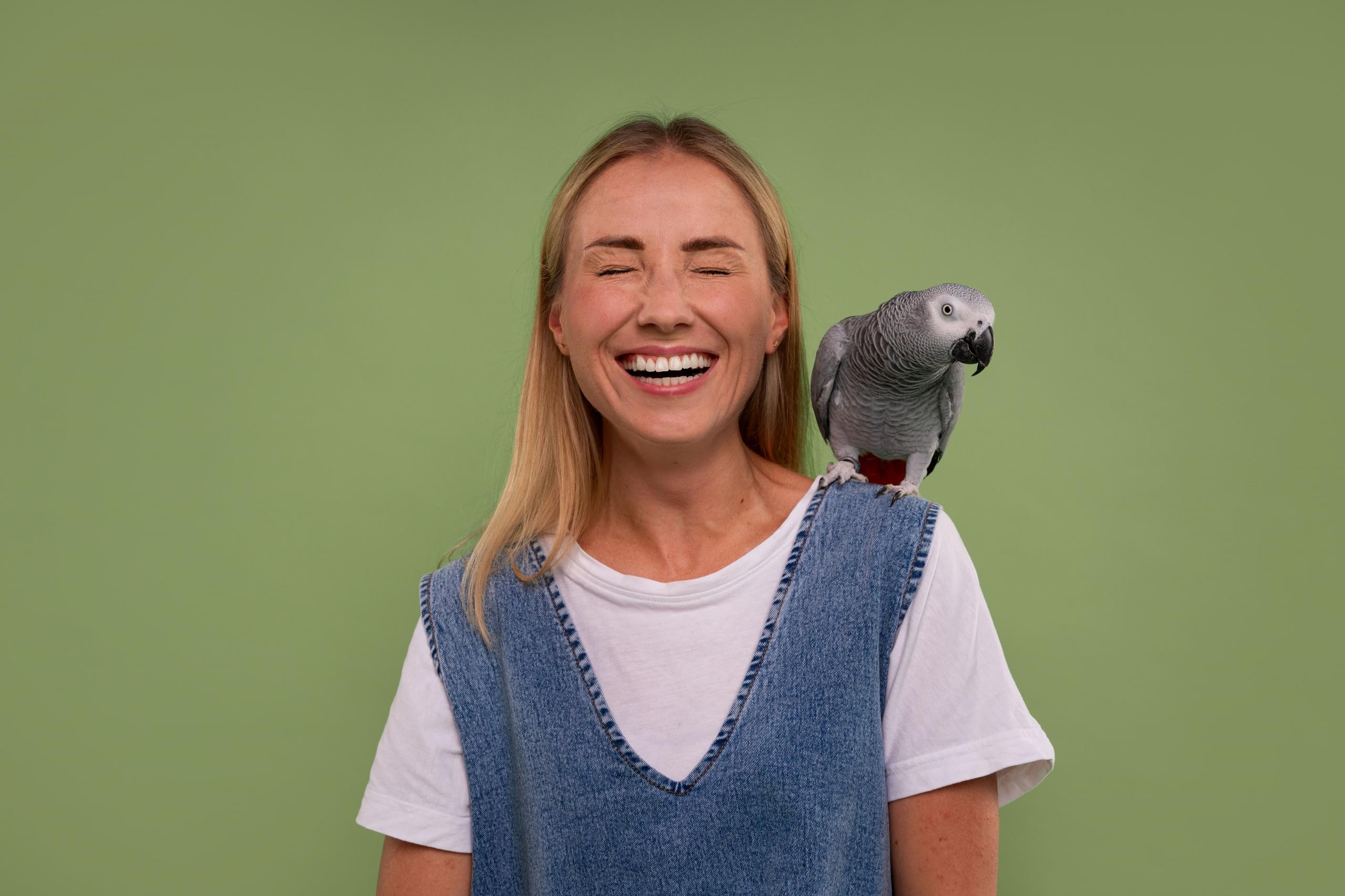chica riendo frente a la cámara con un loro gris en el hombro