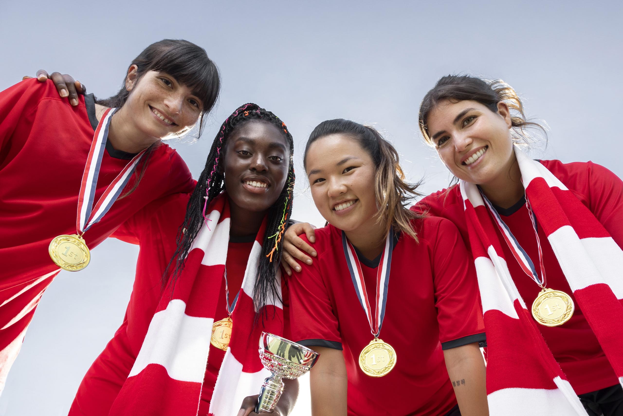 cuatro atletas medallistas sonrientes con uniformes rojo y blanco