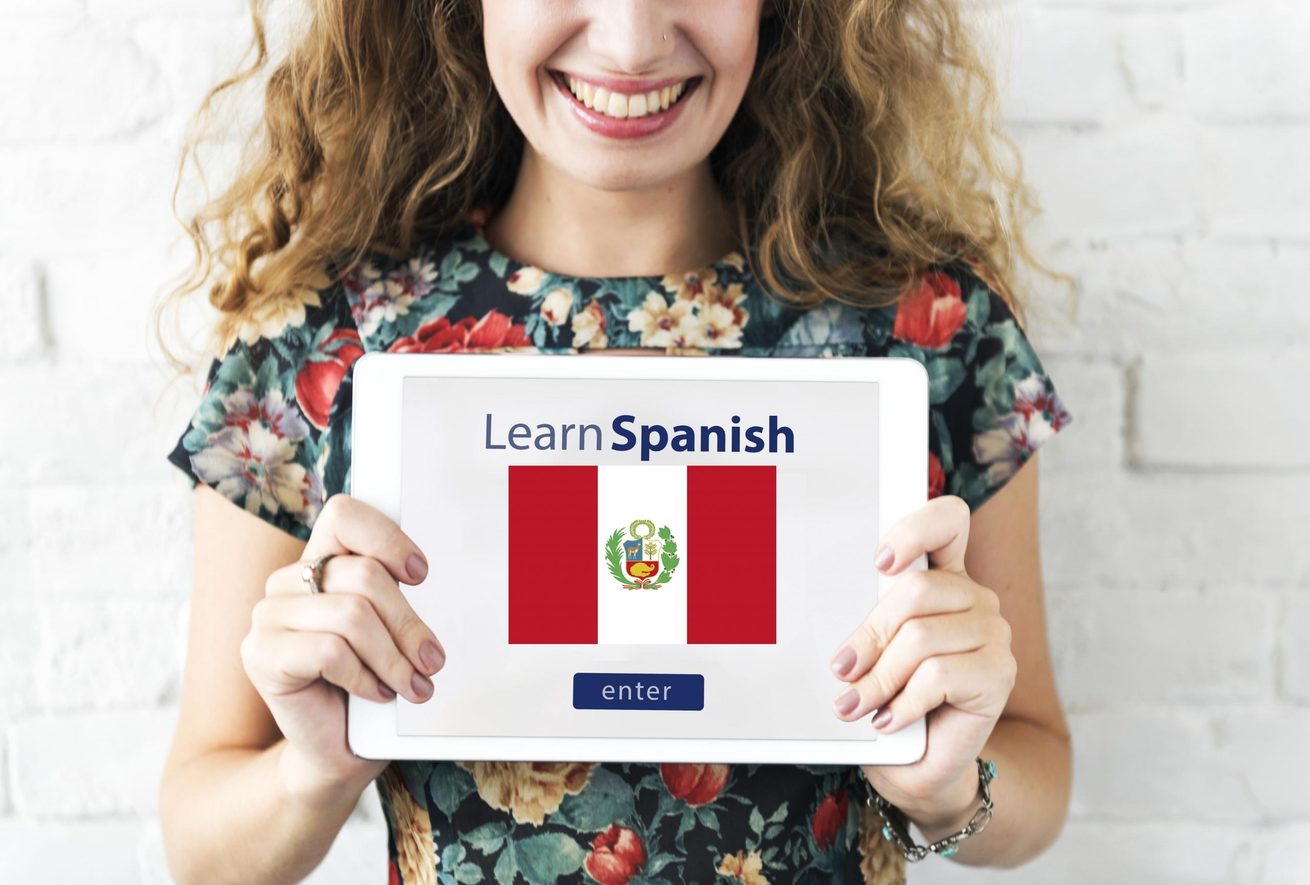 chica sonriente mostrando una tablet con el texto: LEARN SPANISH y la bandera del Perú dentro de la pantalla