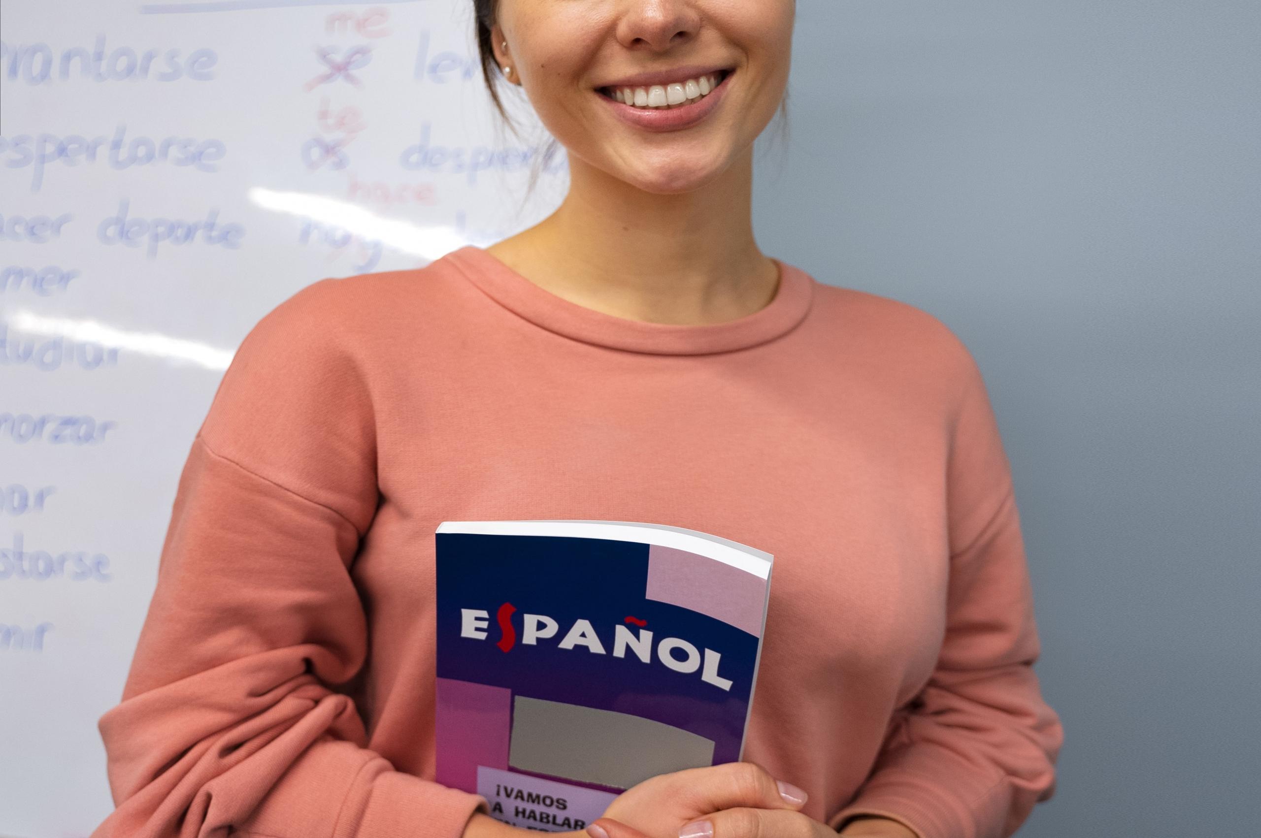 chica sonriente sosteniendo un libro de español contra su pecho