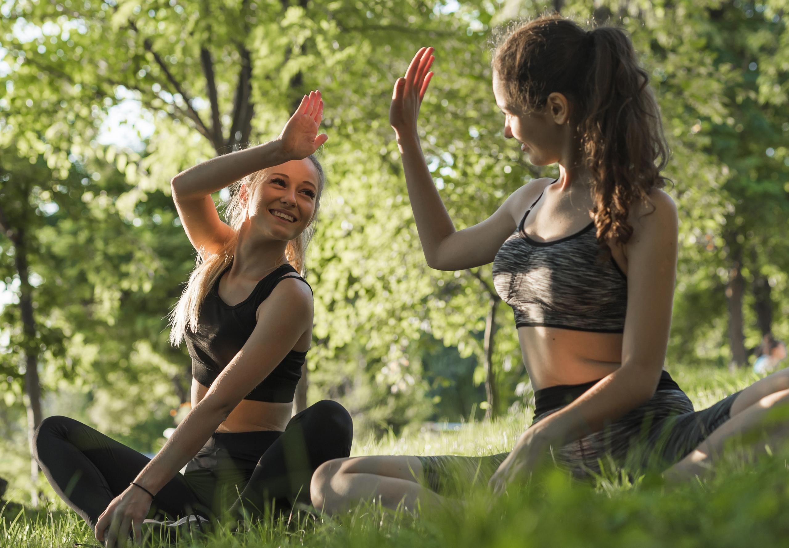 dos chicas chocando las manos sonrientes sentadas en medio del jardin
