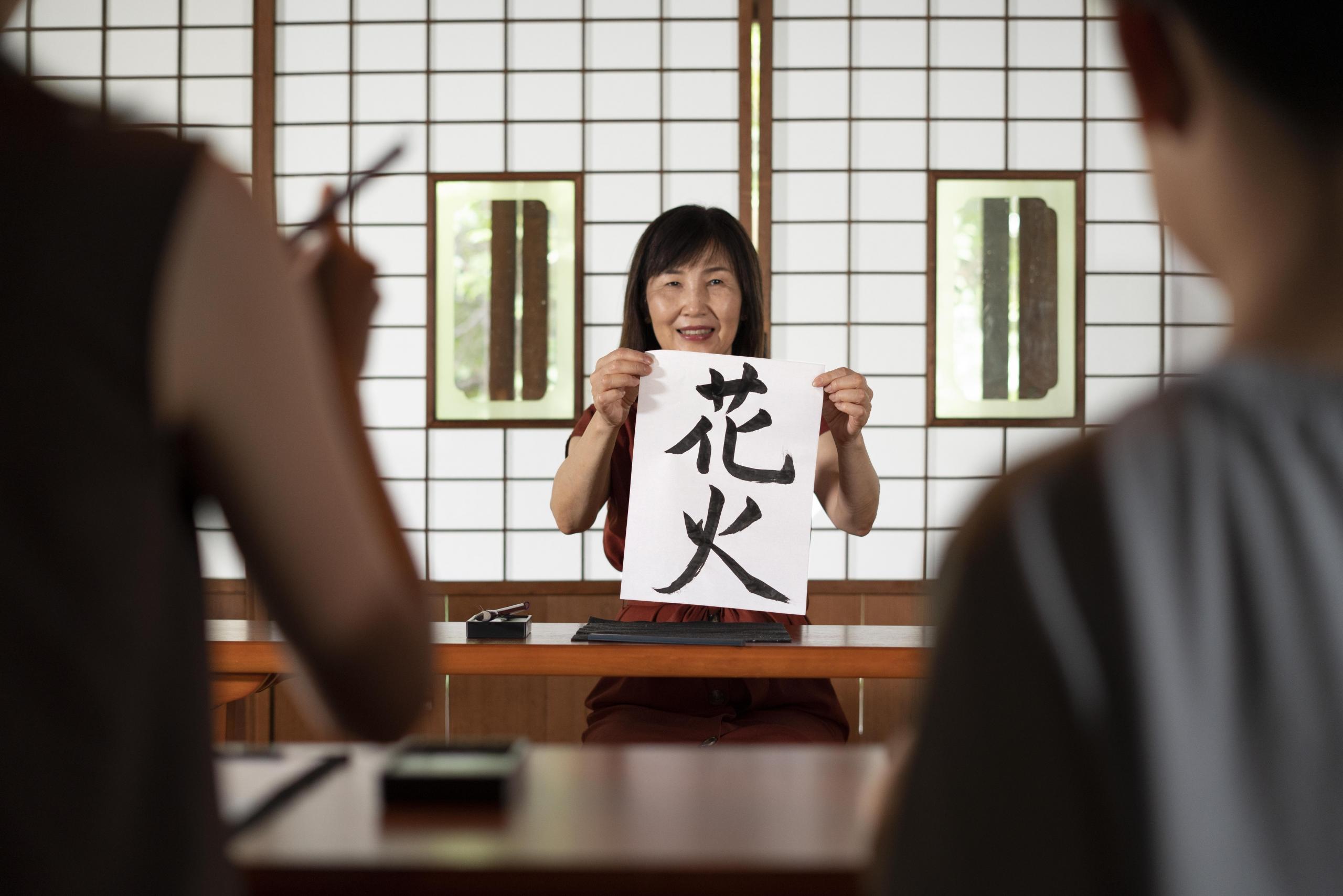 mujer china sosteniendo una hoja con letras chinas mostrándoselo a sus alumnos que están de espaldas a la cámara