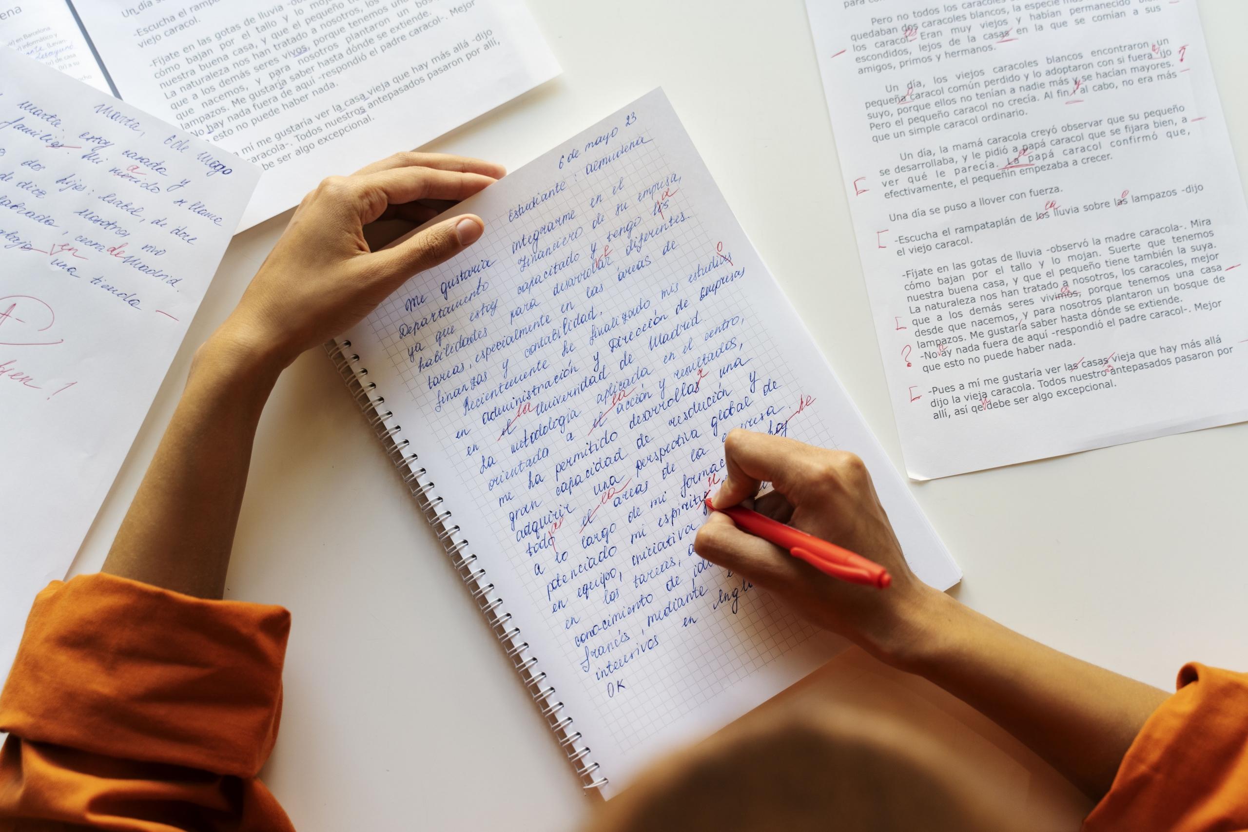 manos corrigiendo unos textos en español escritos con lapicero
