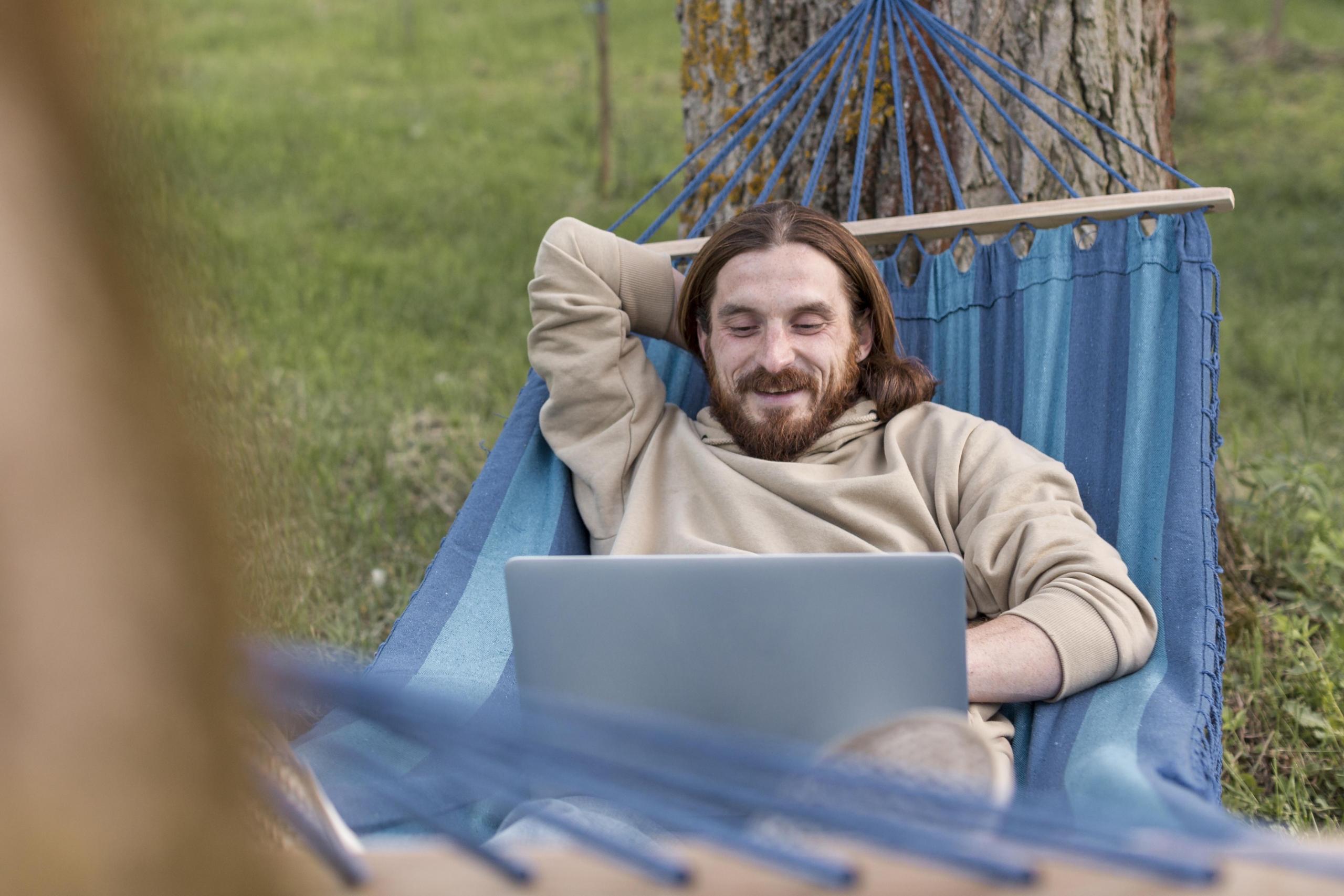 Hombre tirado en una hamaca estudiando por internet 