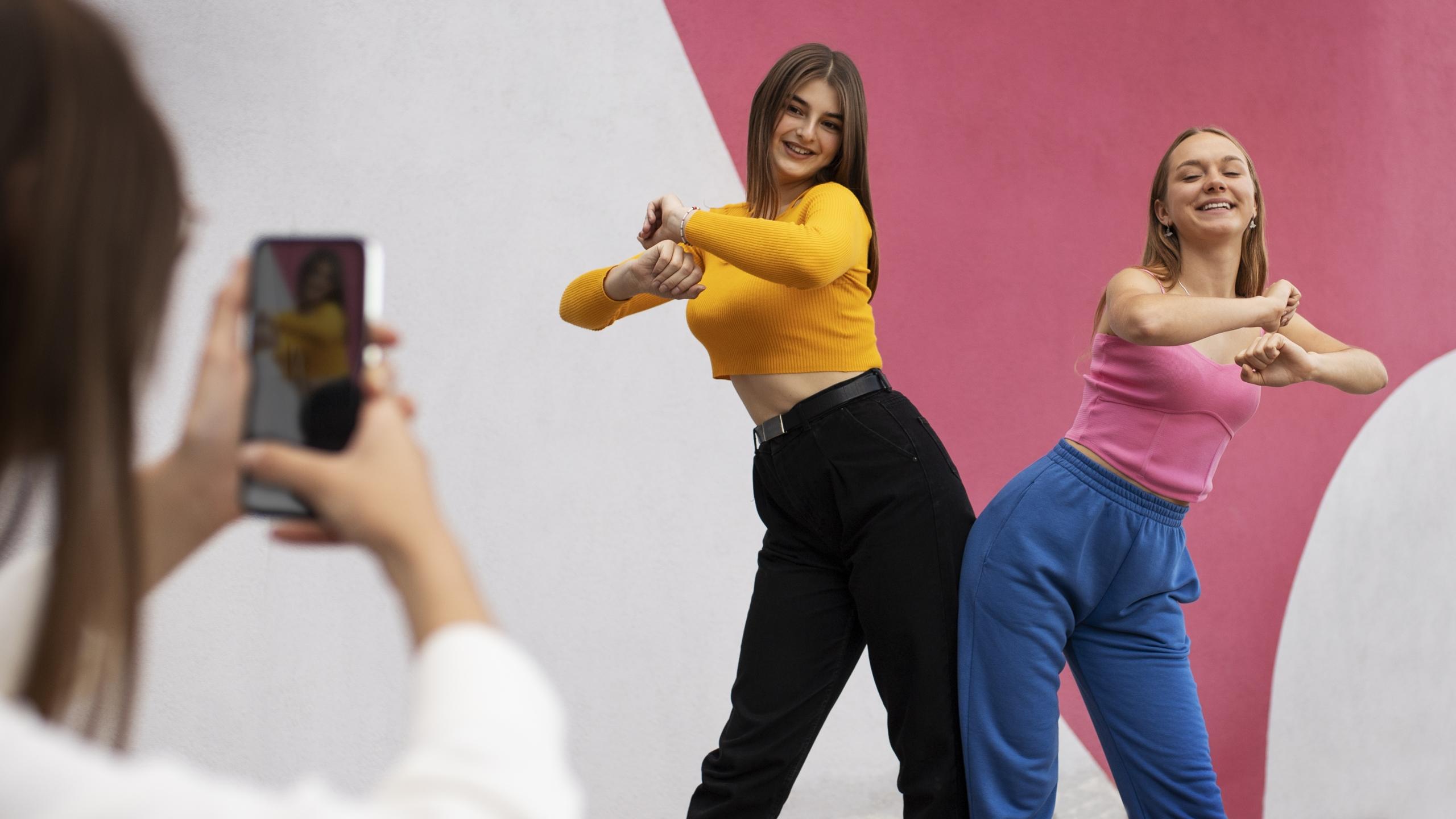 dos chicas bailando a la camara de un celular mientras otra persona las graba