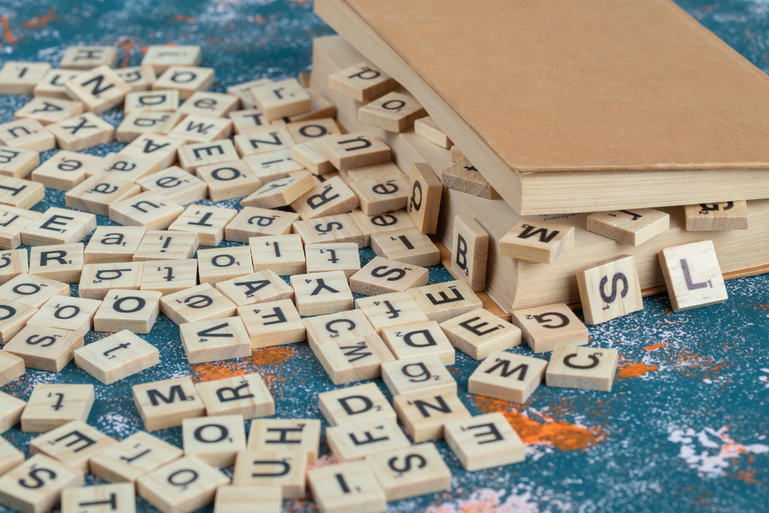 cajita de madera rebalsando de fichas scrabble dispersas por doquier
