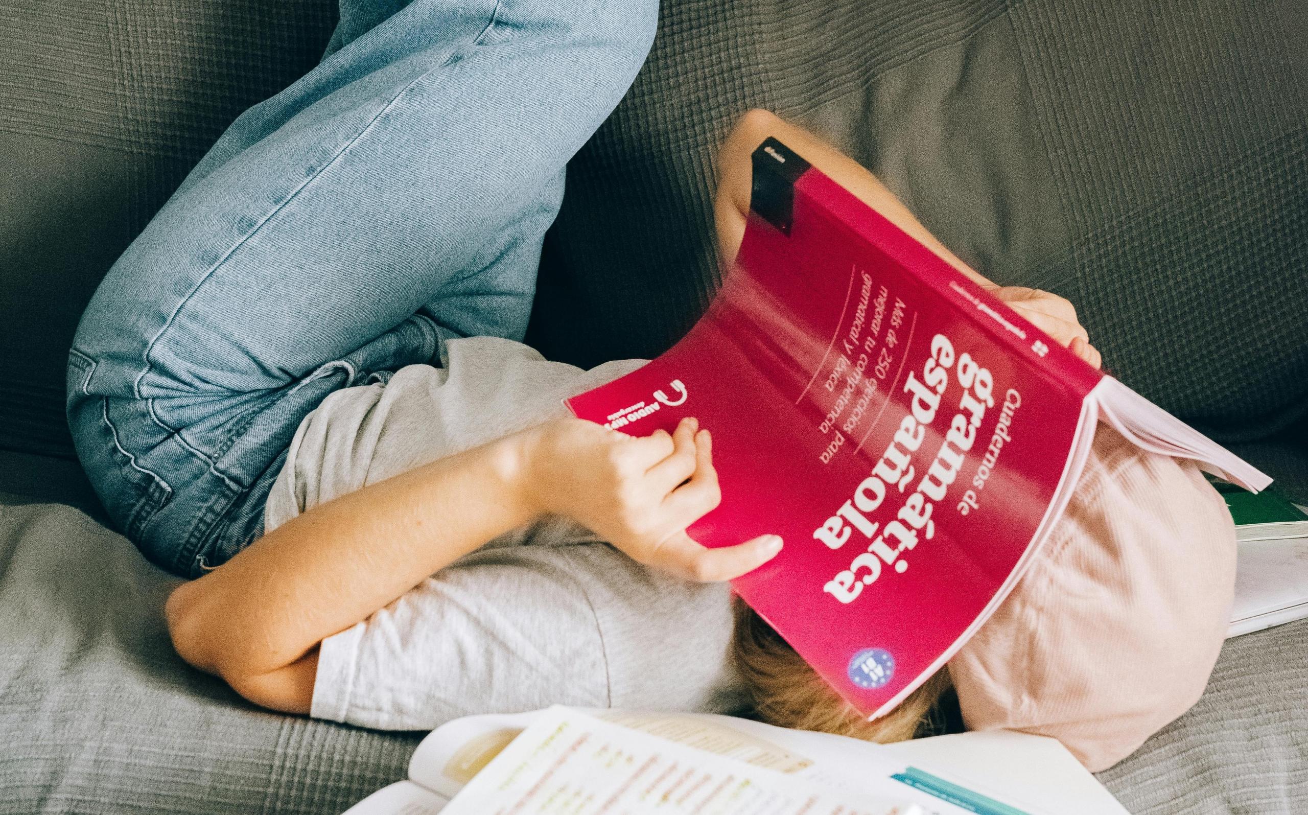 chica echada con un libro rosado de gramatica española tapandole el rostro
