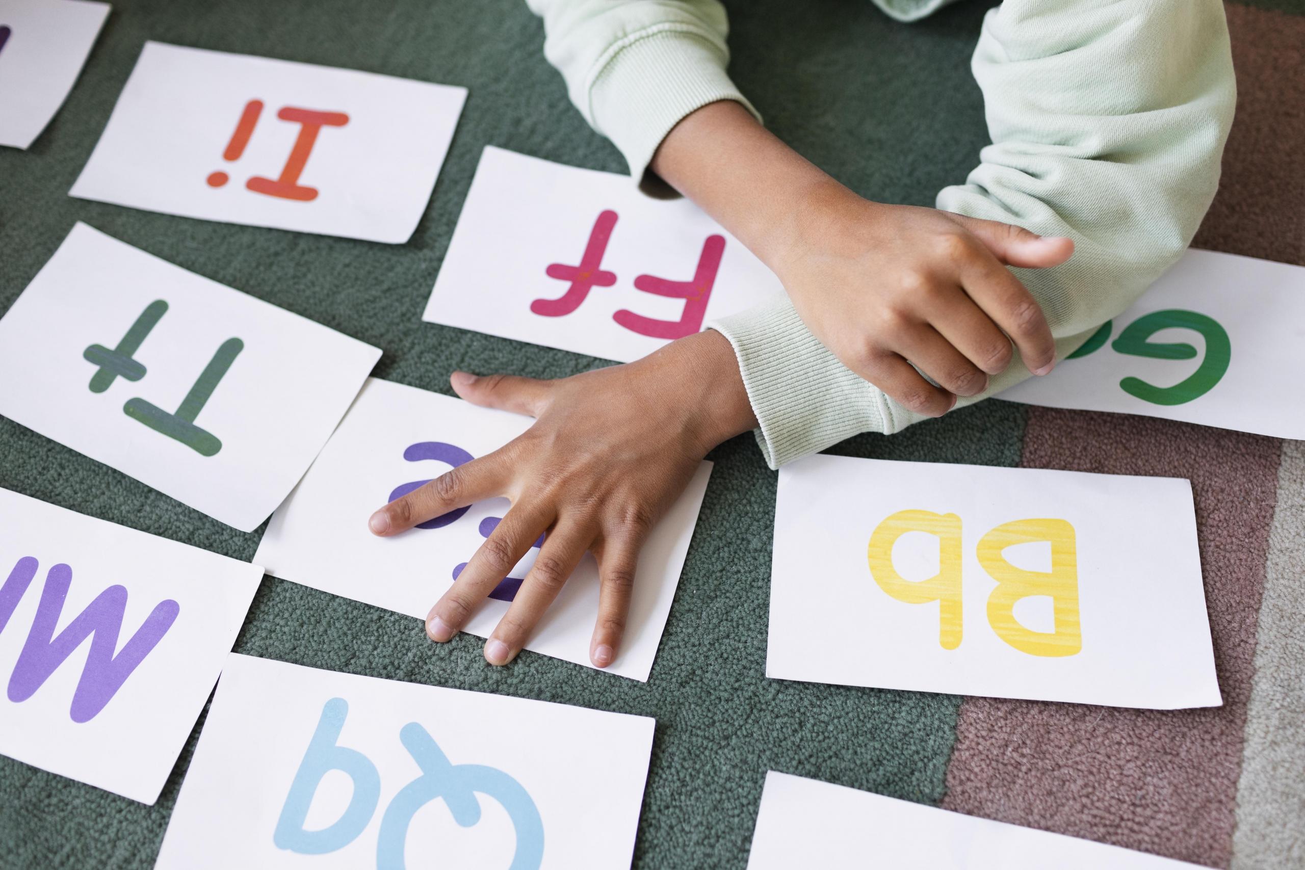 mano de niño sobre unas cartillas didácticas con letras del abecedario en su escritura mayuscula y minuscula