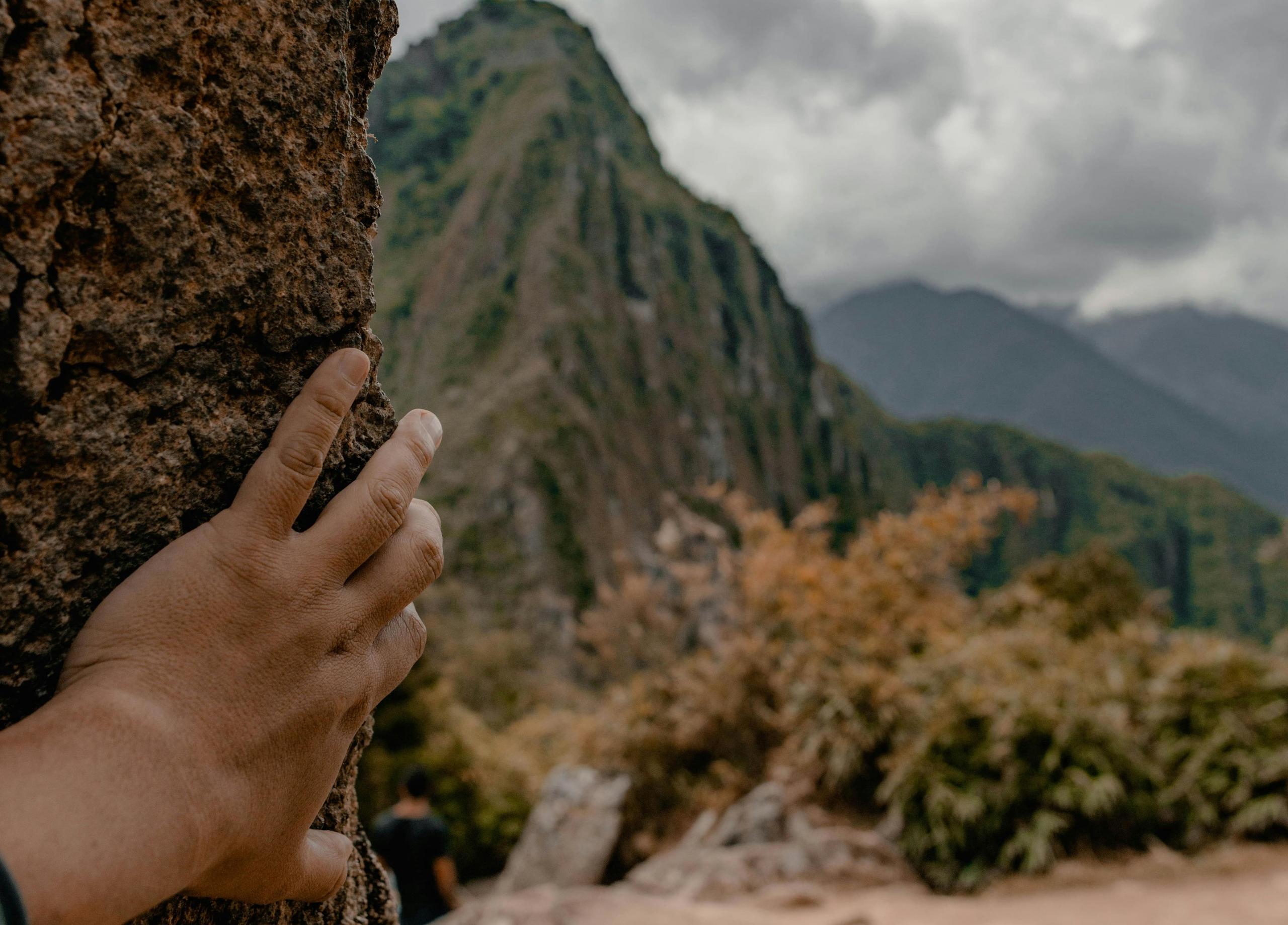 mano asomándose en un muro de piedra viendo una parte de Machu Picchu
