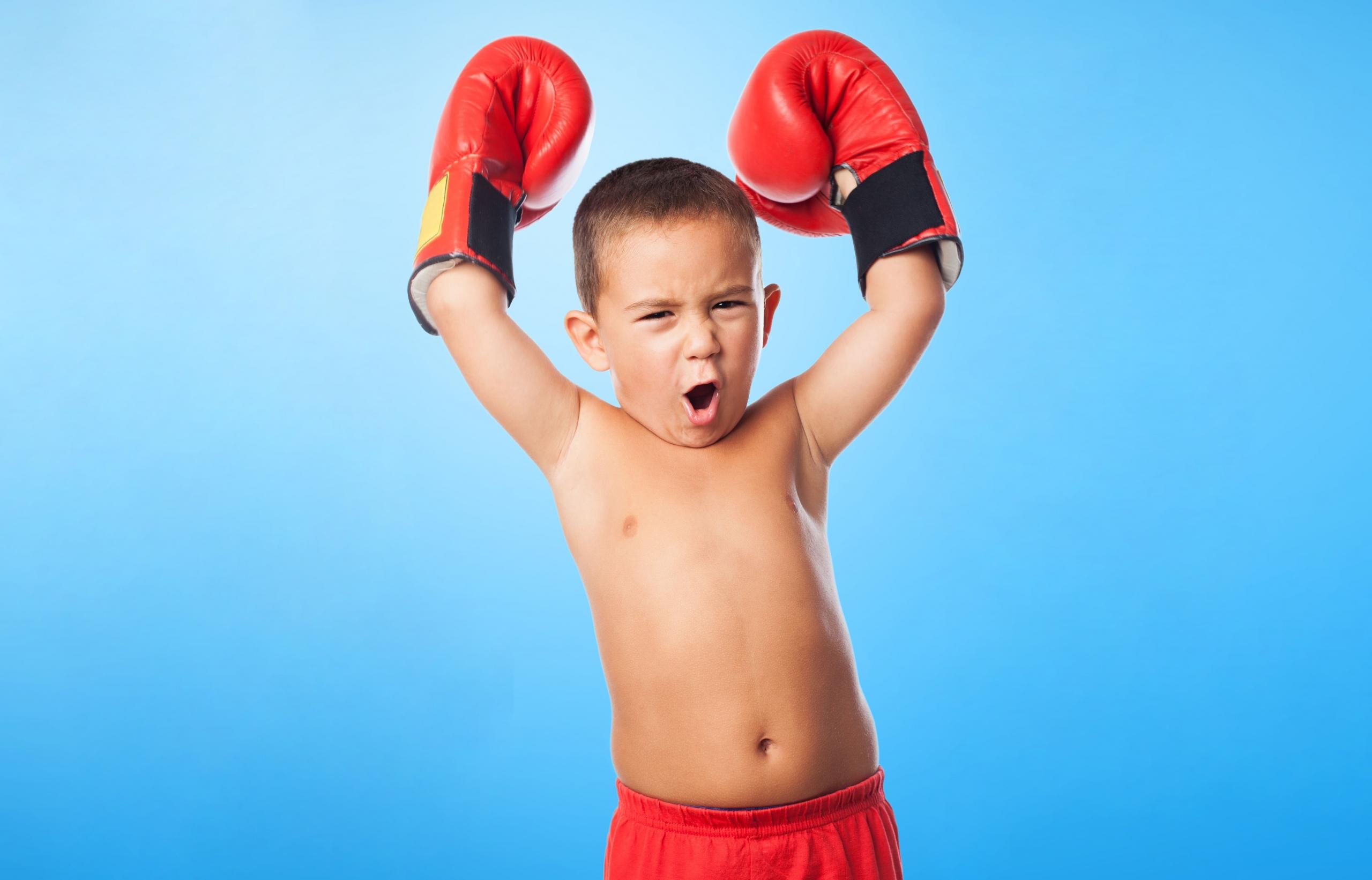niño con shorts y guantes de box con grito feliz y brazos elevados