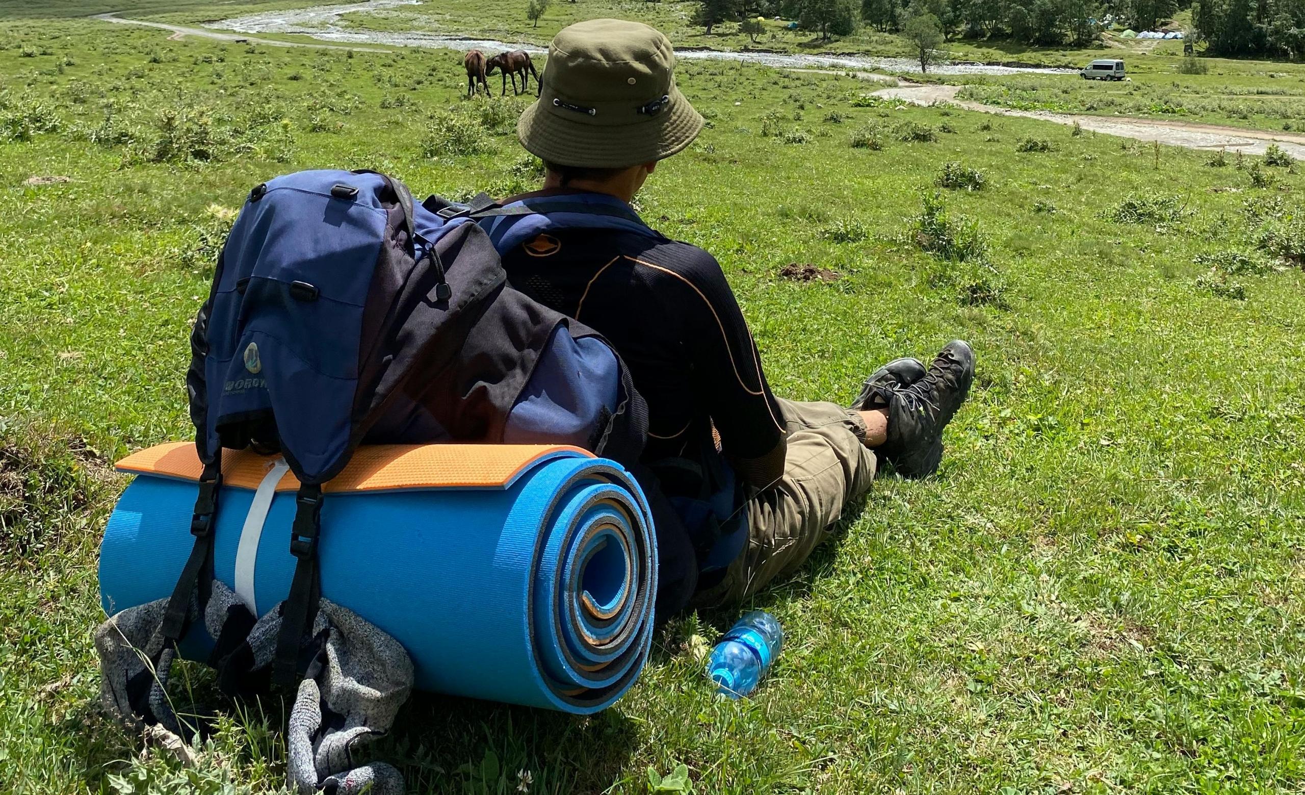 chico con equipaje de aventura sentado mirando el campo