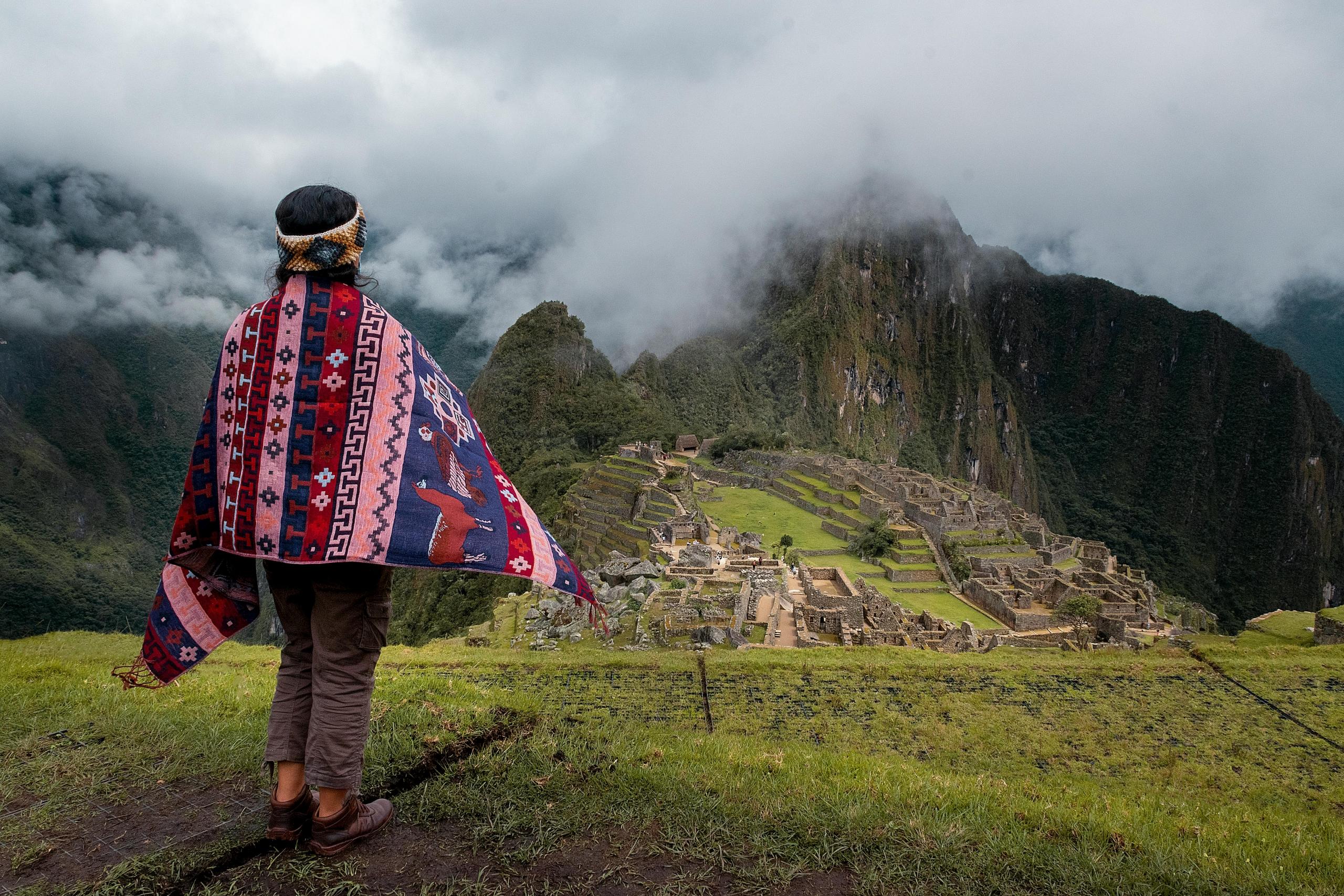 chica de espaldas con manto cusqueño mirando hacia Machu Picchu