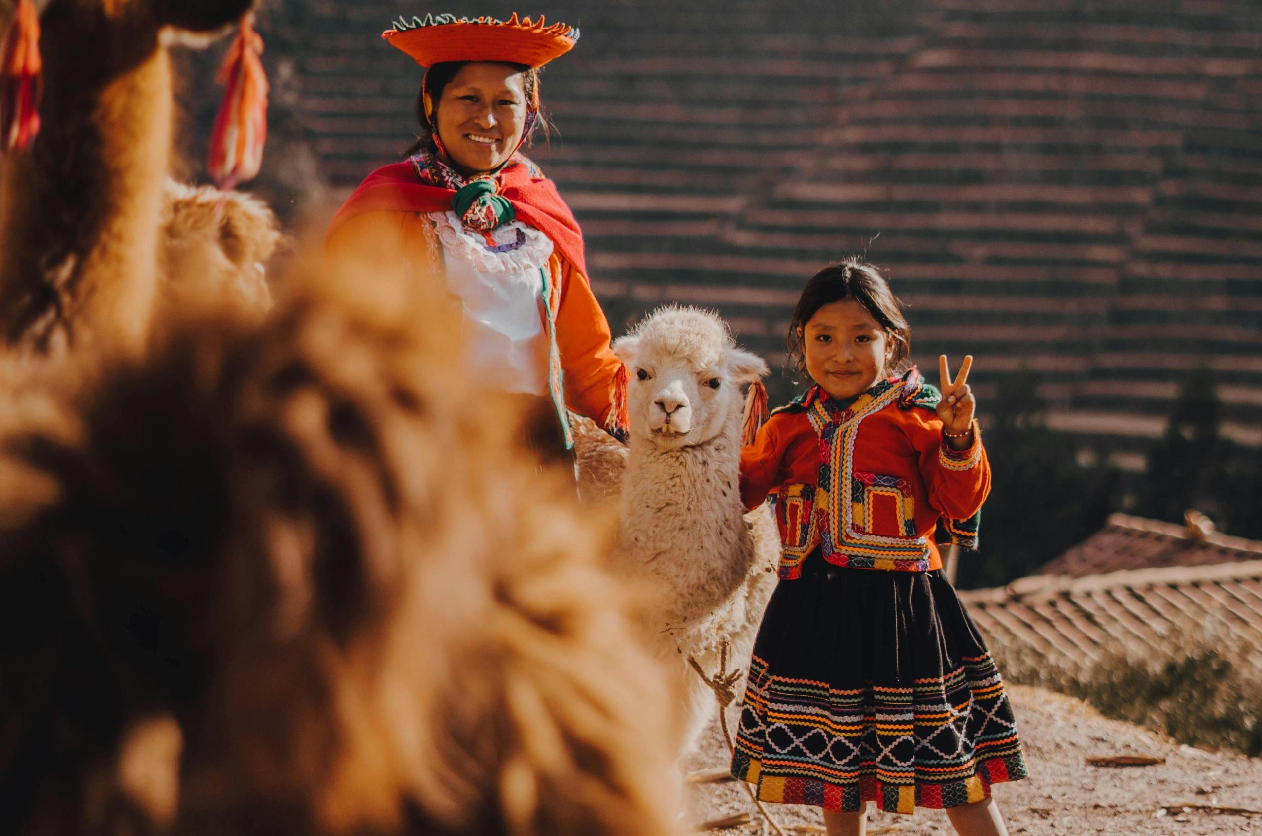 mujer y su hija con trajes tipicos cusqueños junto a una alpaca sonriendo a la cámara