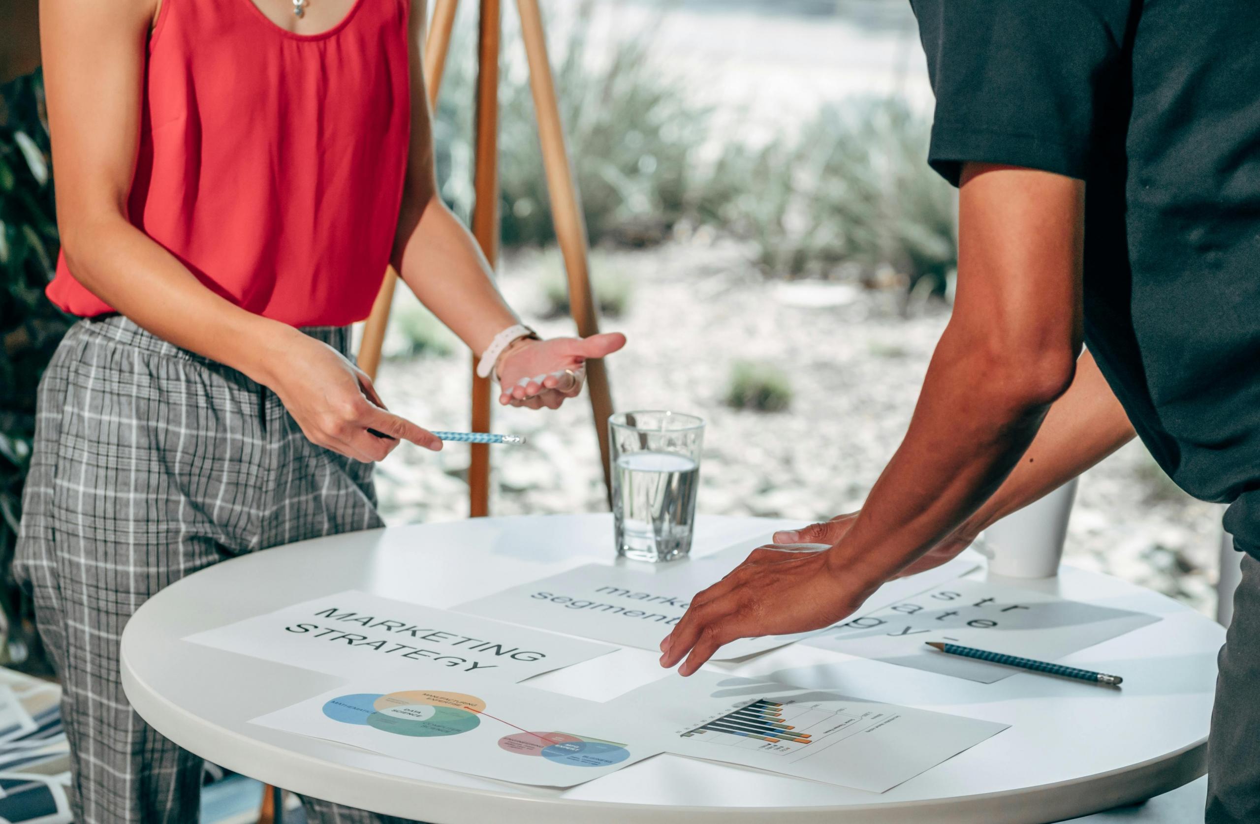 dos personas discutiendo una presentación con hojas de marketing sobre la mesa
