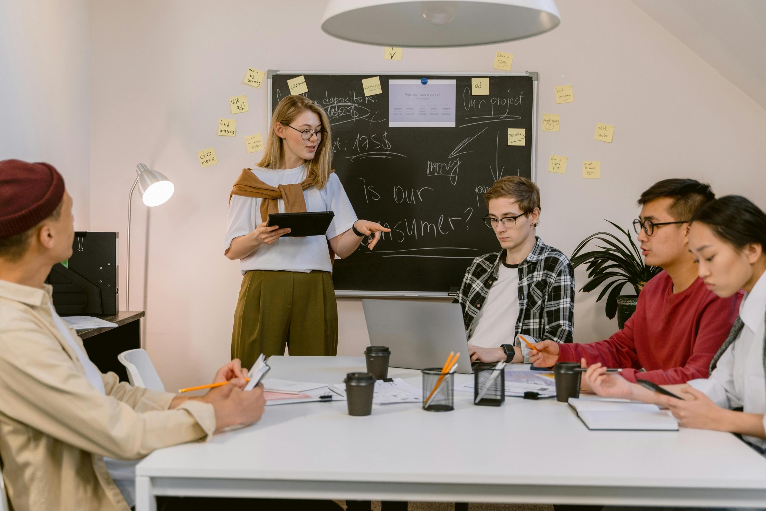 grupo de personas trabajando con una laptop y pizarra llena de ideas y preguntas