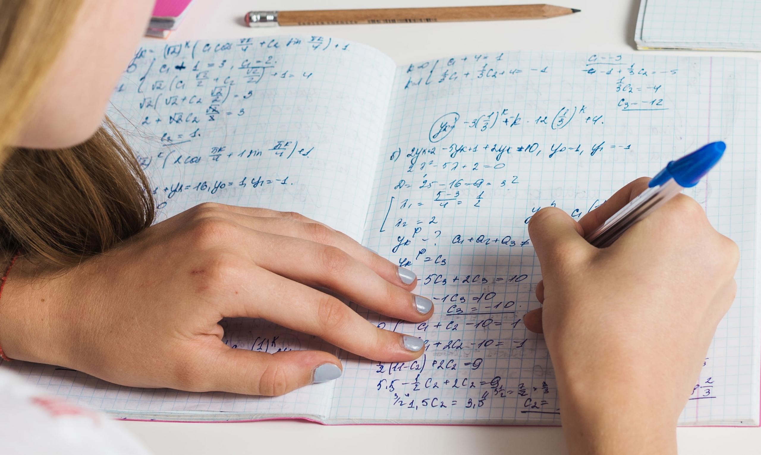 vista de las manos de una niña resolviendo problemas matemáticos a mano en su cuaderno