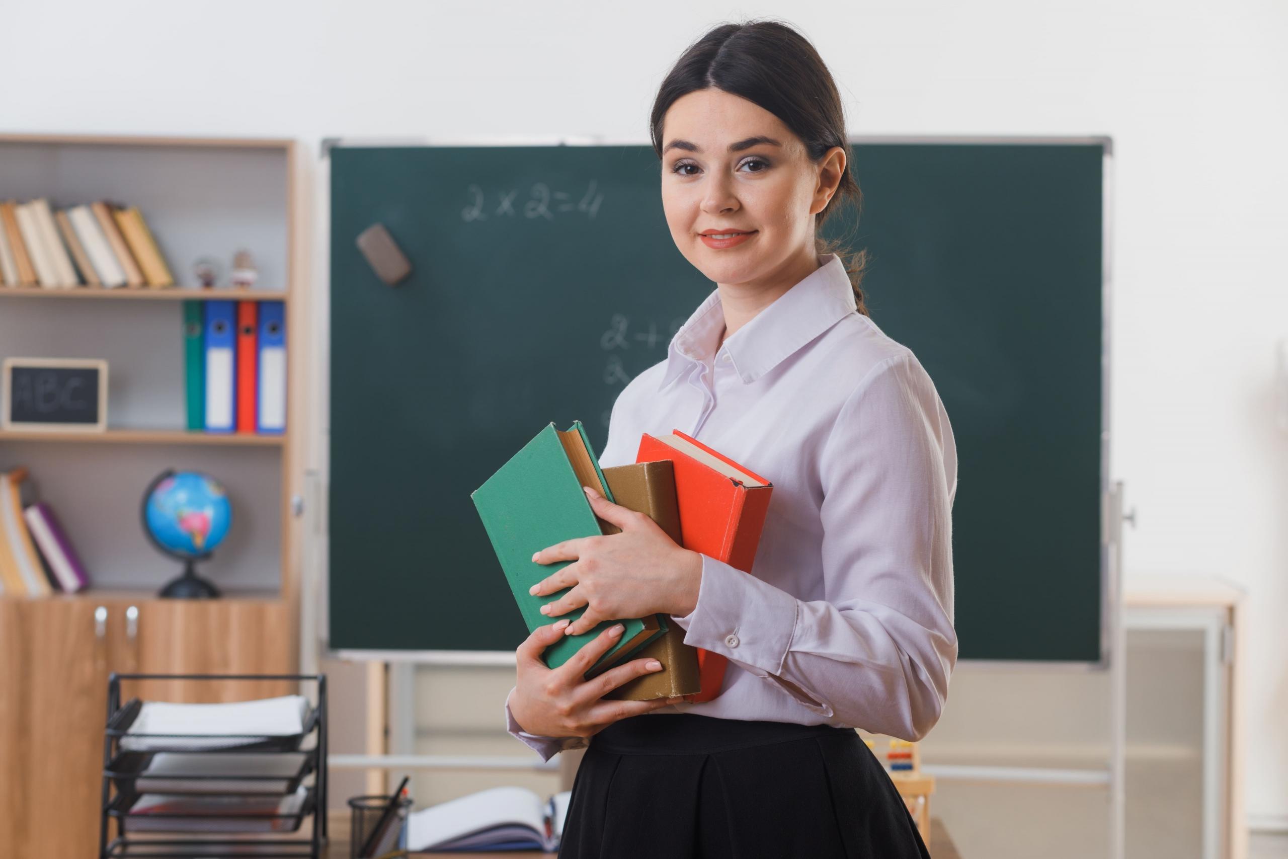 profesora con libros entre los brazos con fondo de salon de clase