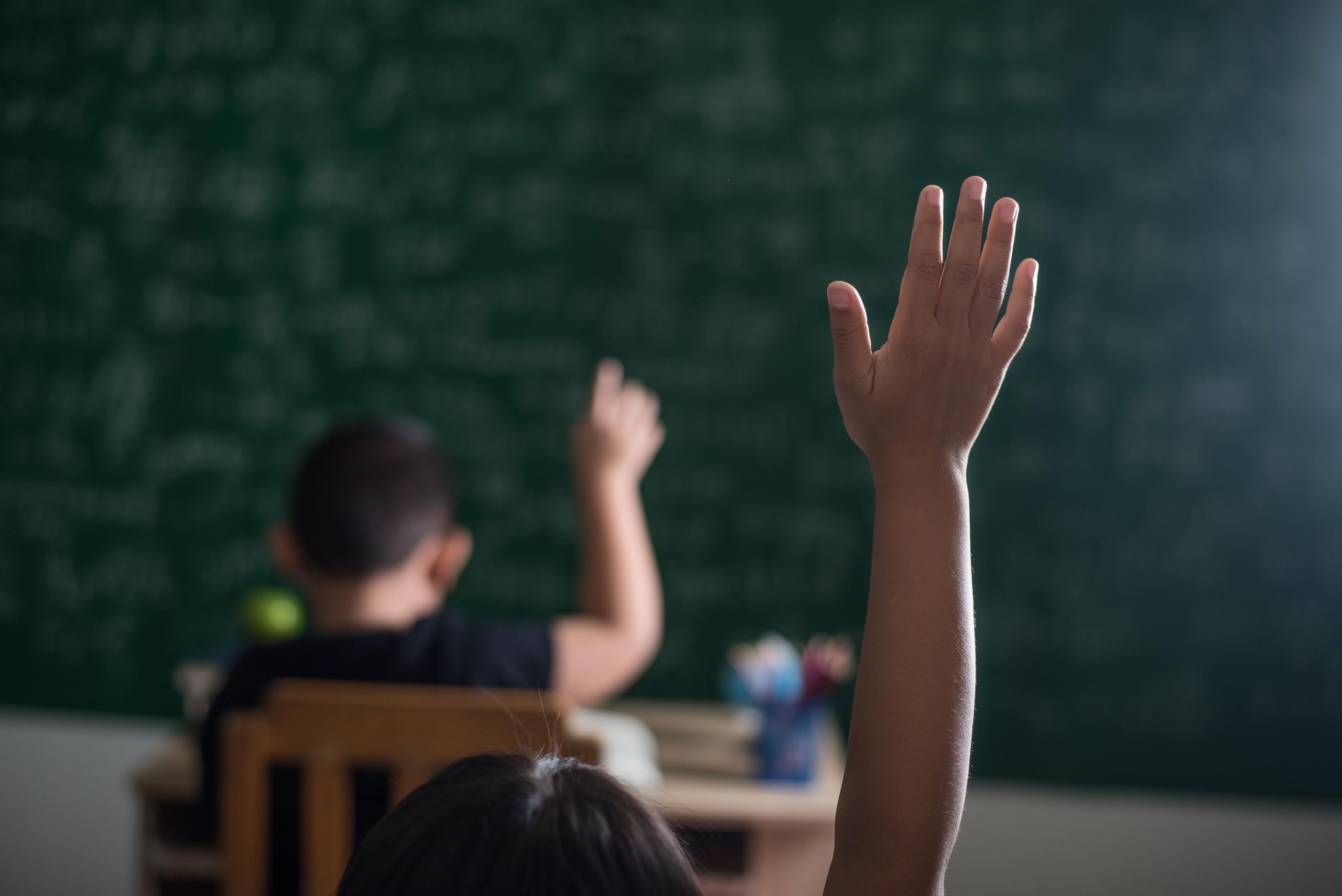 mano de niño levantada en clase con fondo desenfocado