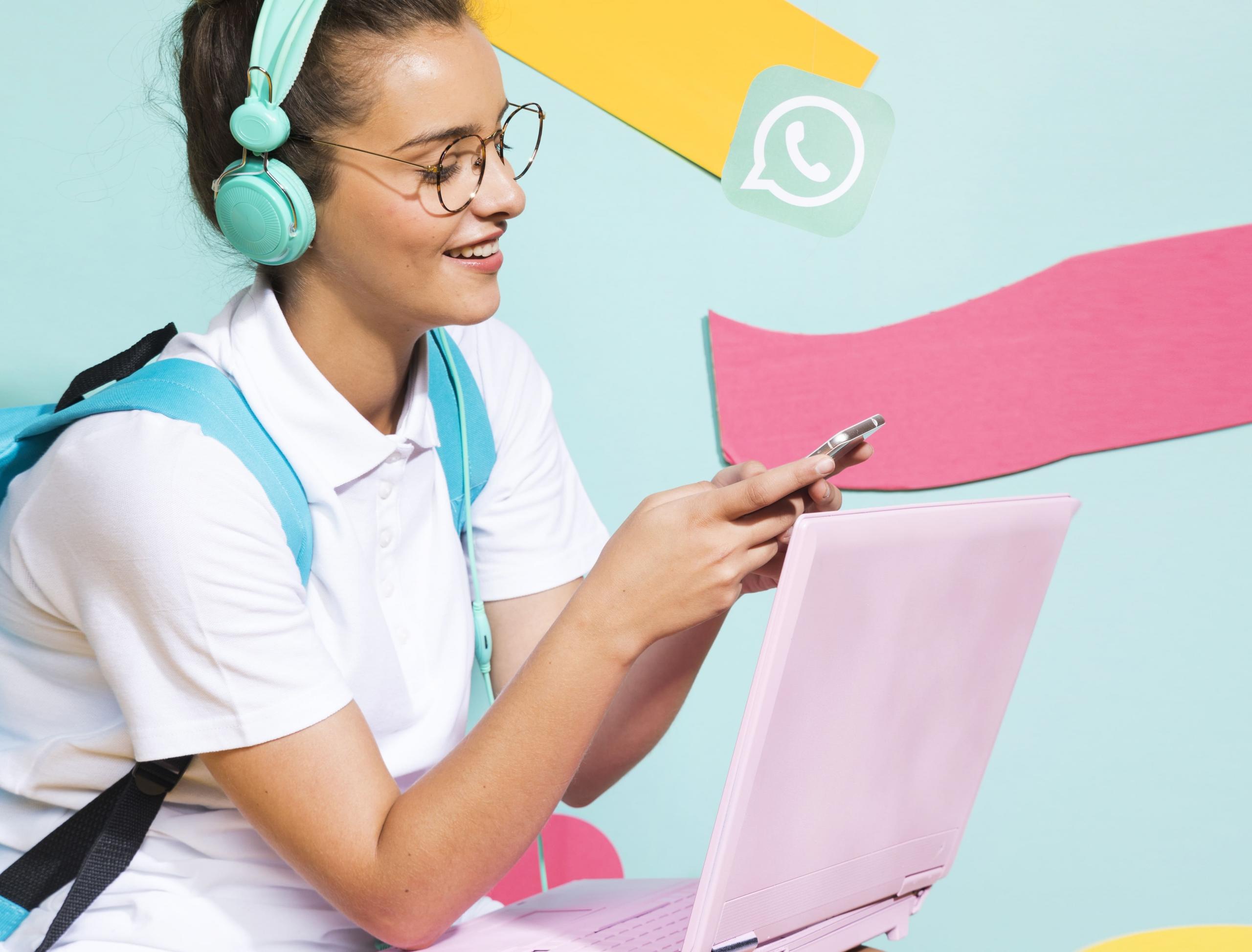 chica mirando su celular junto a una laptop rosada e icono de whatsapp