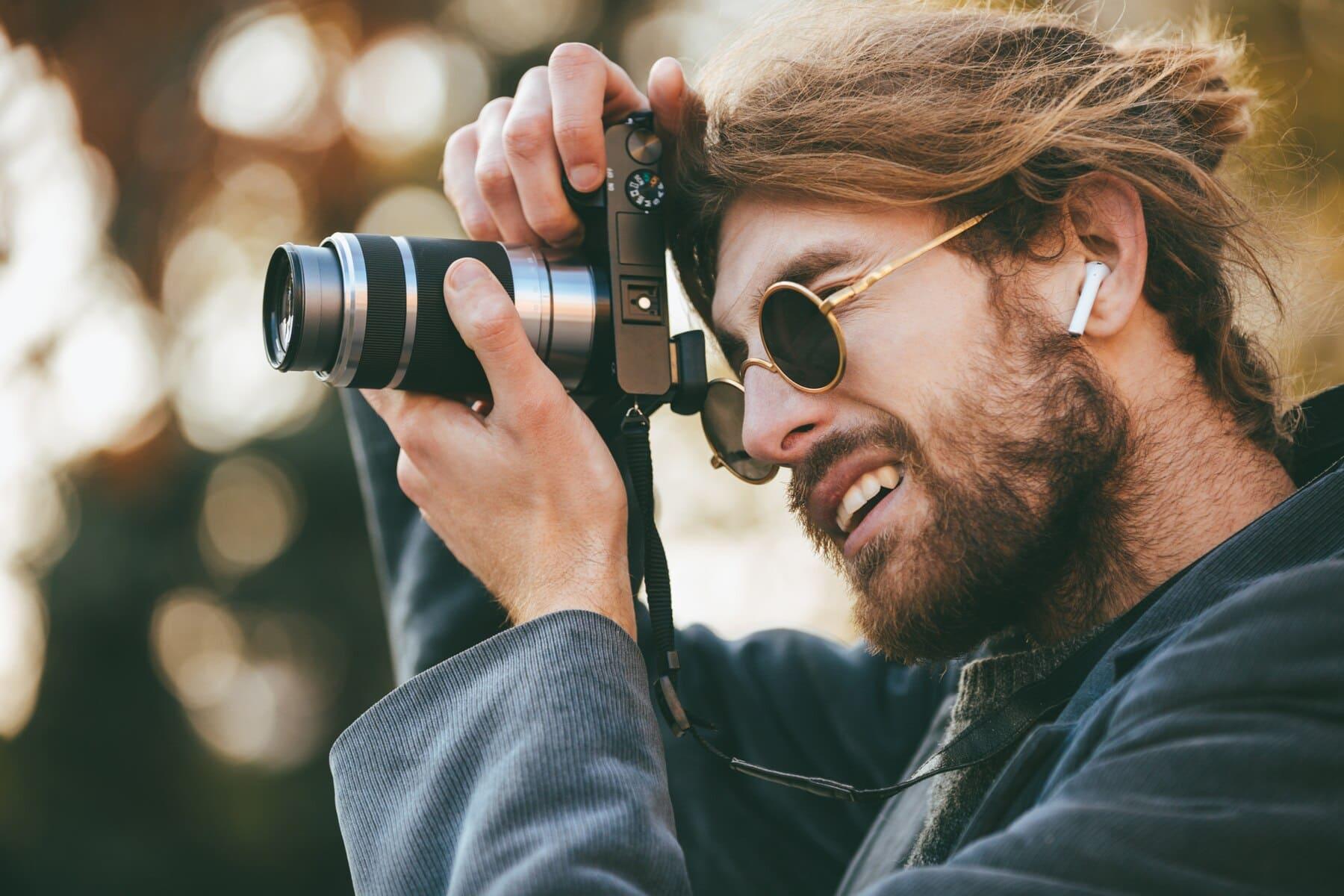 vista de chico de perfil tomando una foto con su cámara y lentes negros en la calle