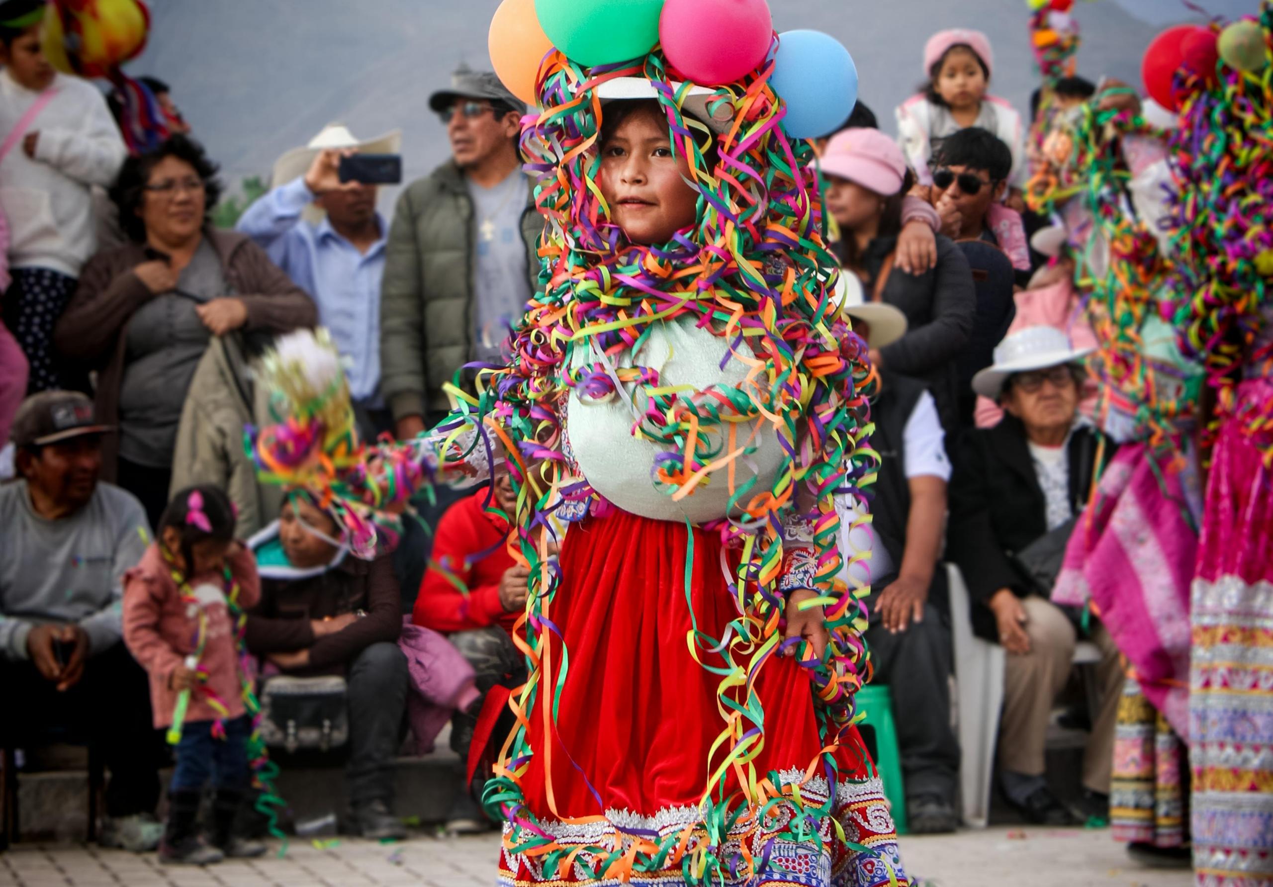 niña con traje típico de carnal cubierta de serpentinas y globos en medio del público